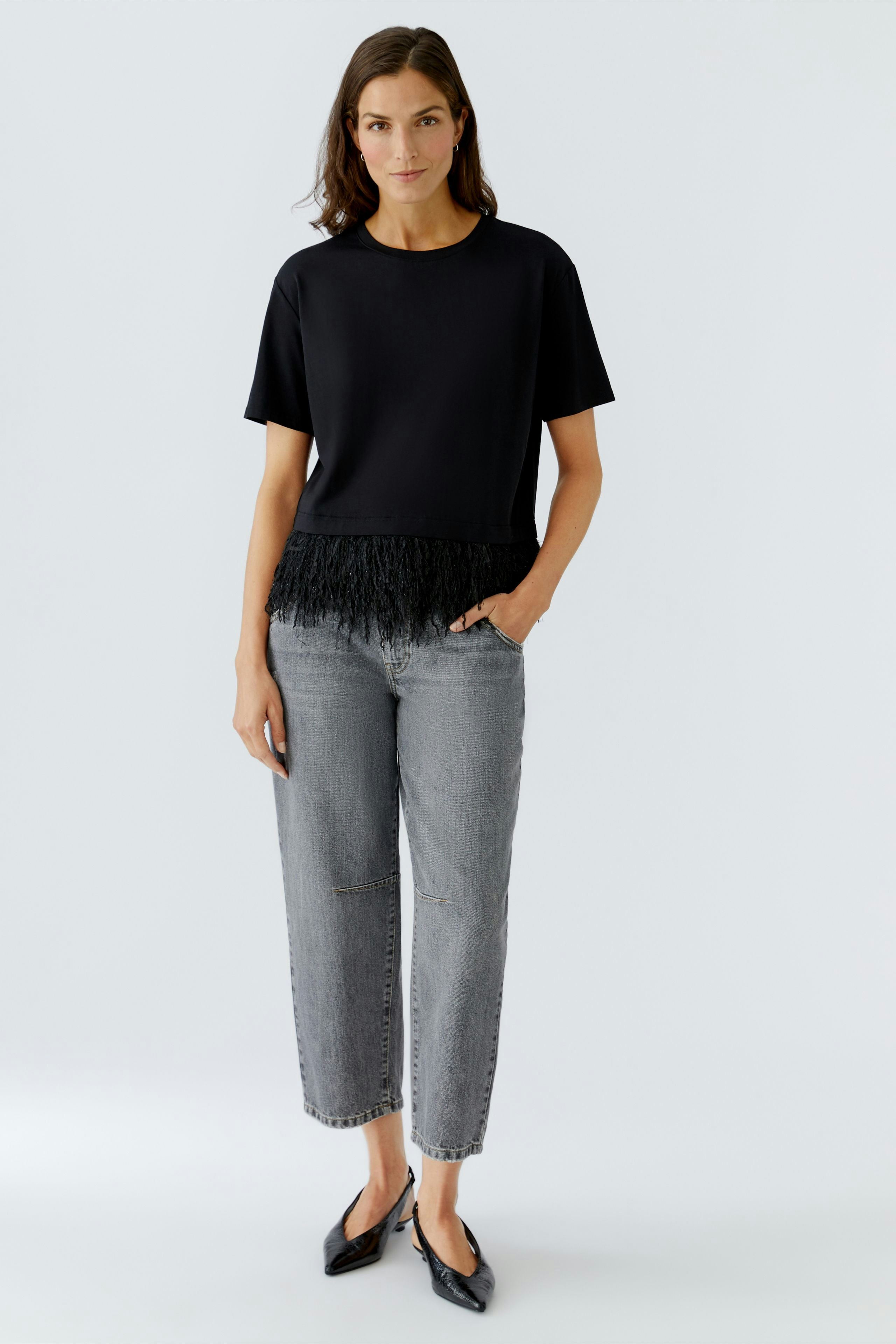 Casual women's T-shirt: Woman in a black top with fringe detail, paired with gray jeans.