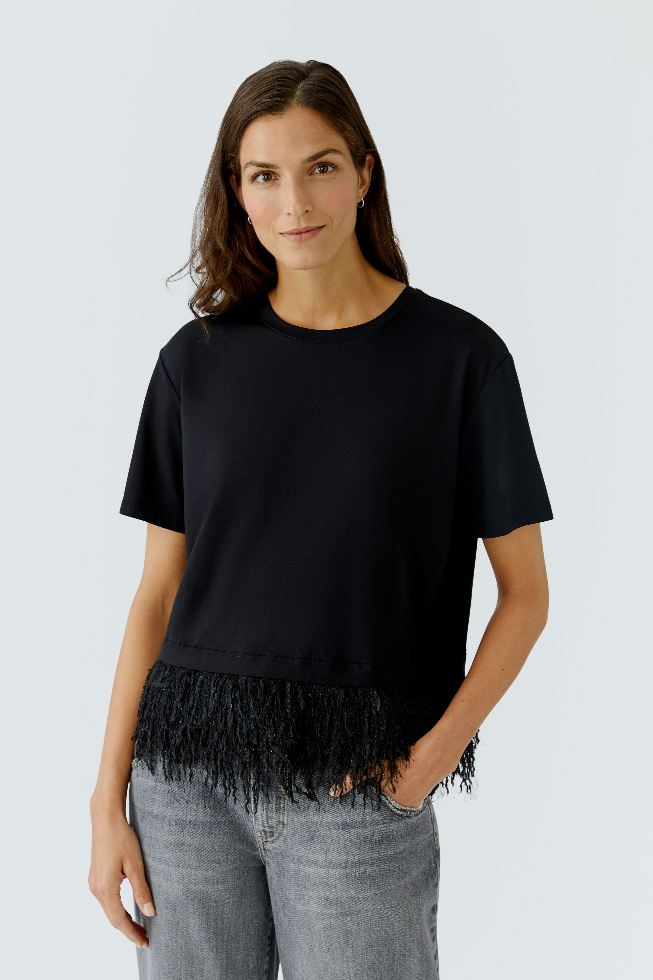 Casual women's T-shirt: Woman in a black top with fringe detail, paired with light jeans.