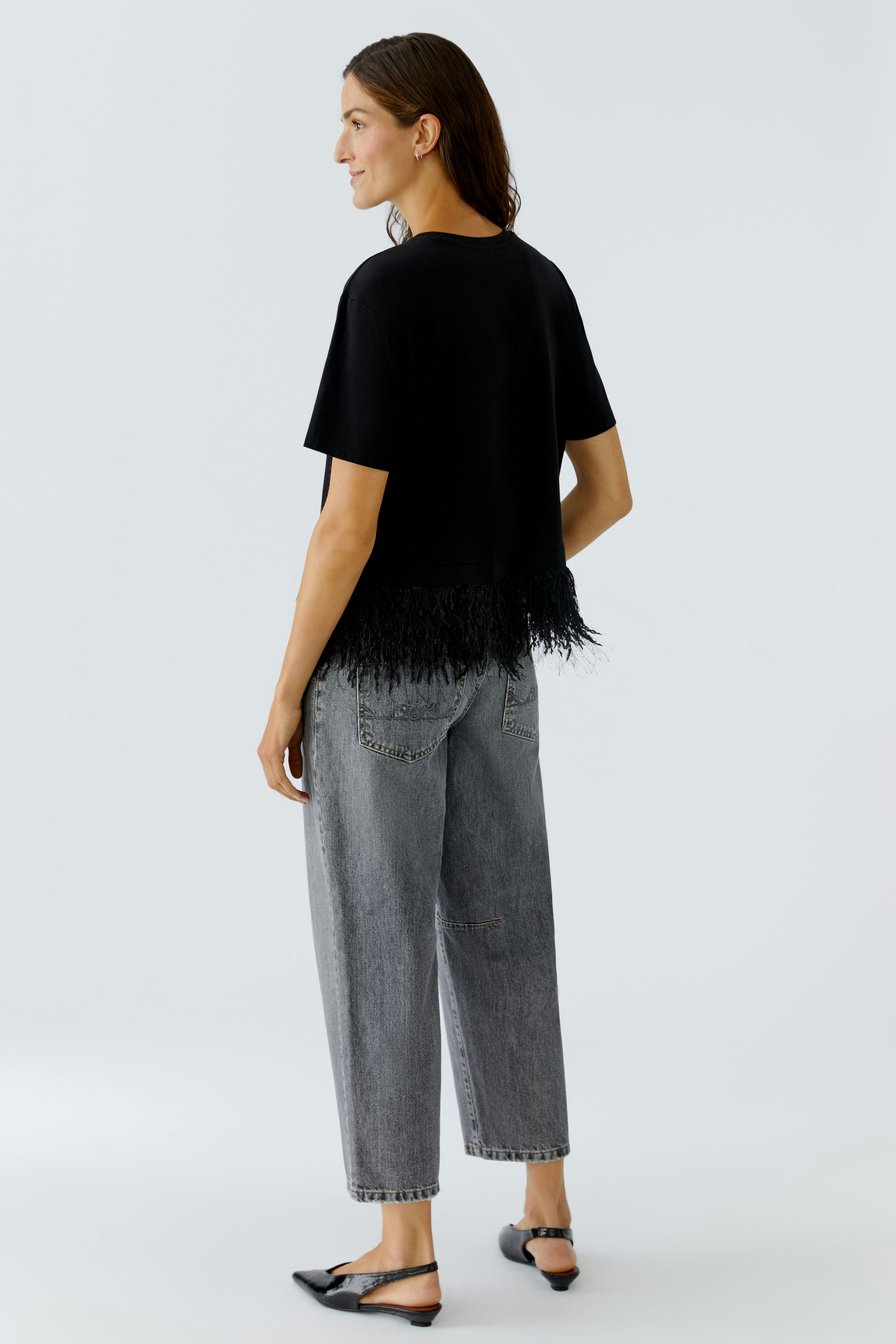 Casual women's T-shirt: A woman in a black tee with fringe detail, paired with relaxed-fit jeans.