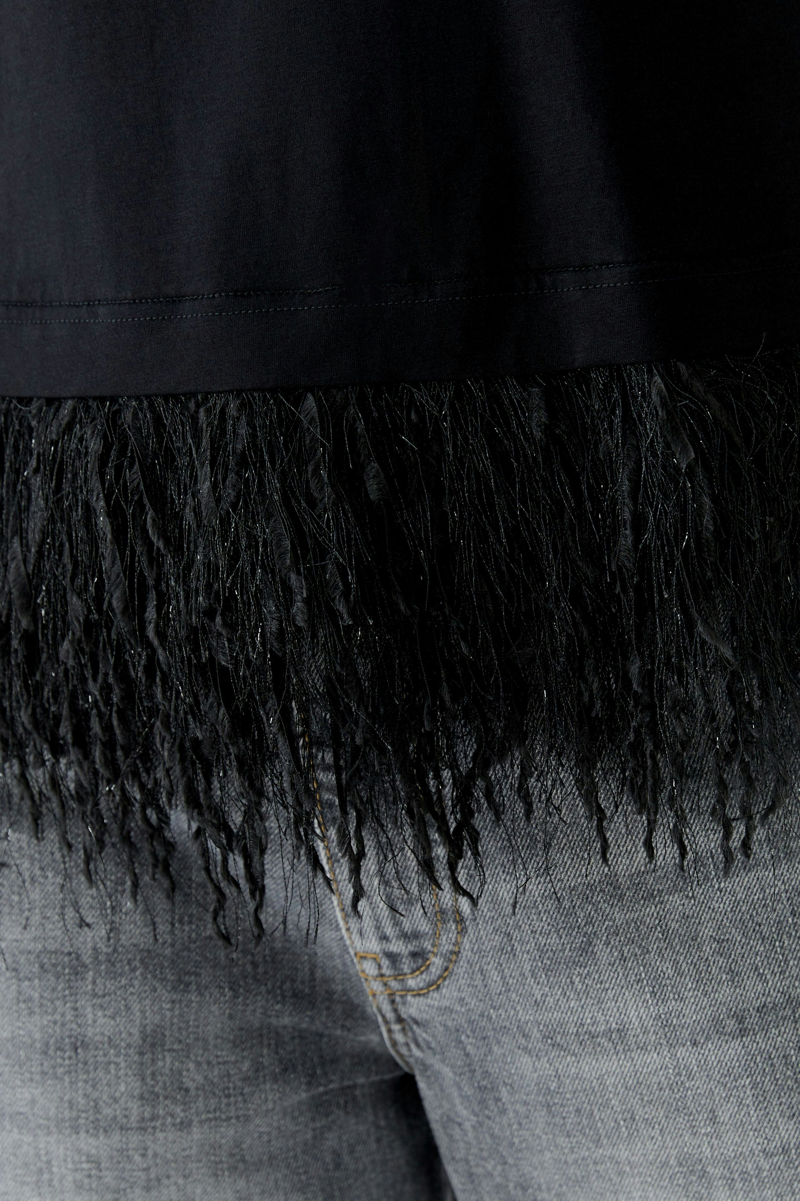 Casual women's T-shirt with a fringed hem, paired with jeans for a relaxed look.