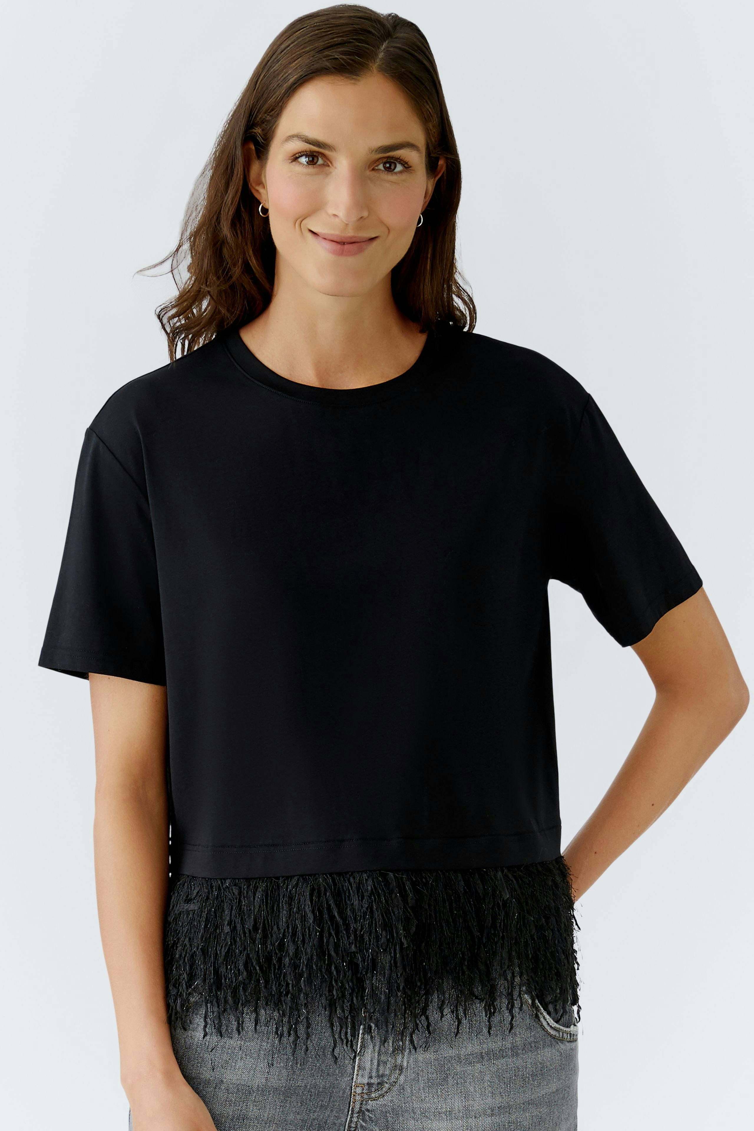 Casual women's T-shirt: A woman in a black tee with fringe detailing, paired with jeans.