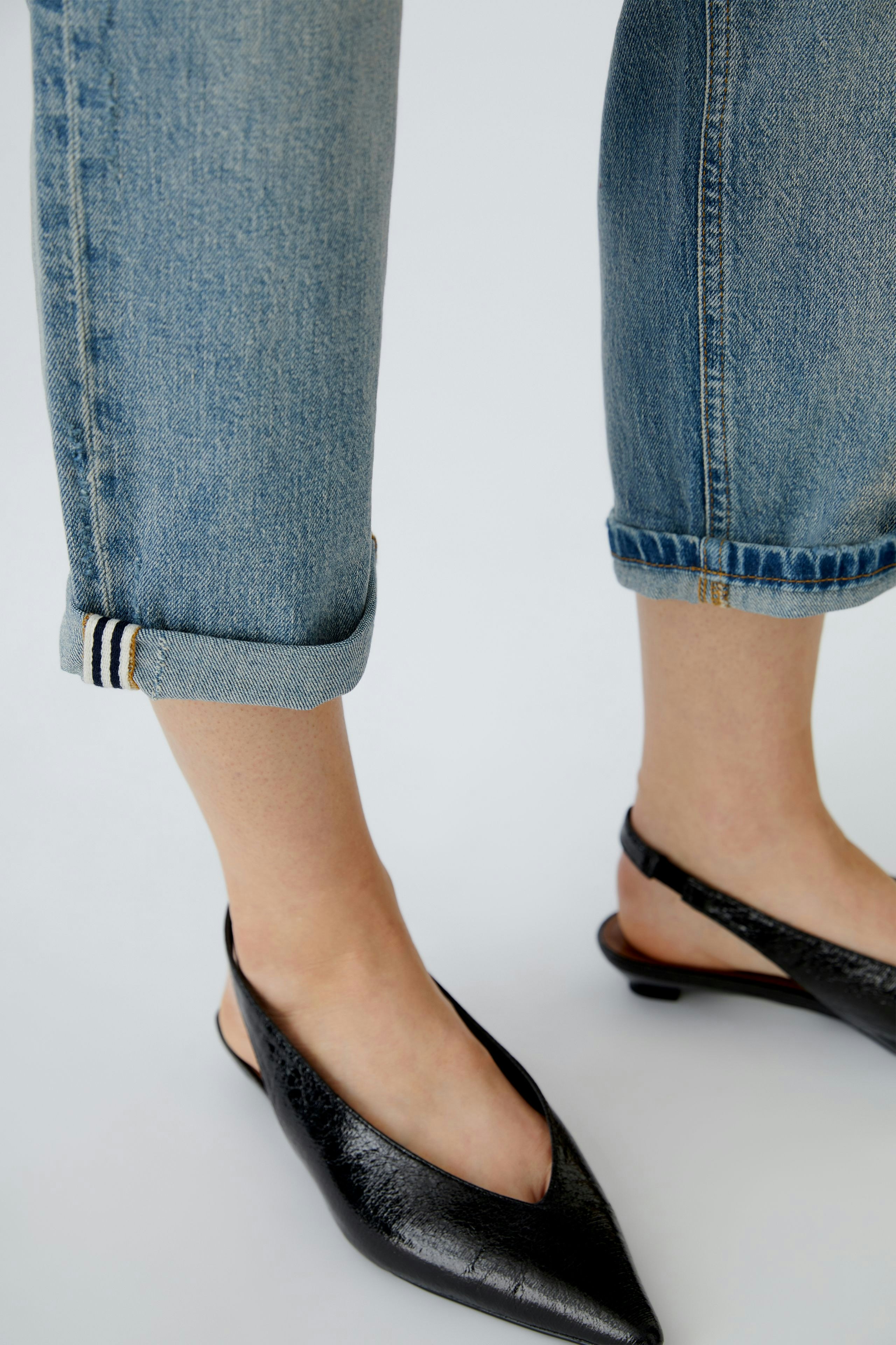 Bequeme Damen-Jeans: Frau trägt lässige, hellblaue Jeans mit umgeschlagenem Saum und schwarzen Sling-Pumps.