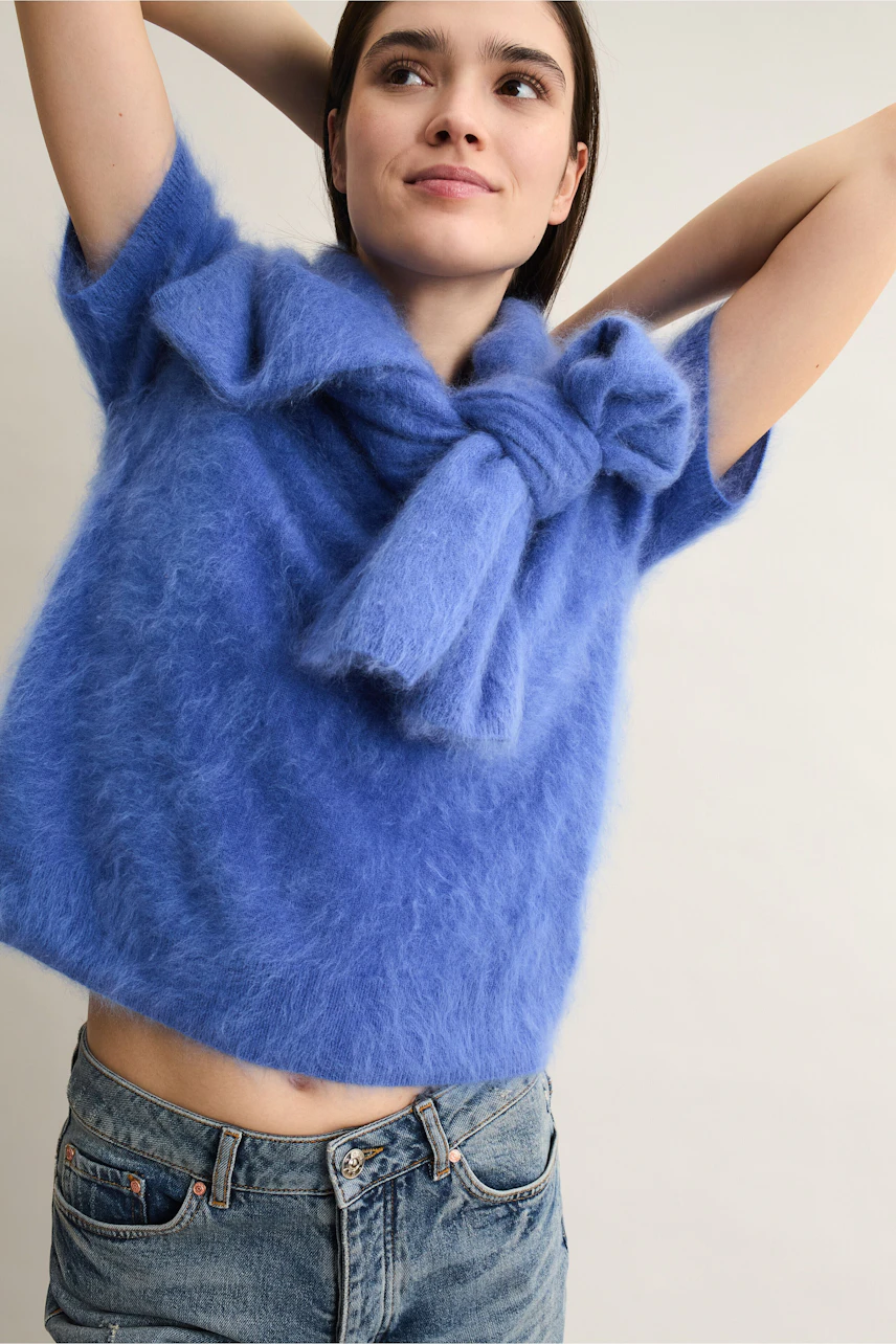 Casual women's pullover: Young woman in a blue fluffy pullover with a bow detail, smiling confidently.