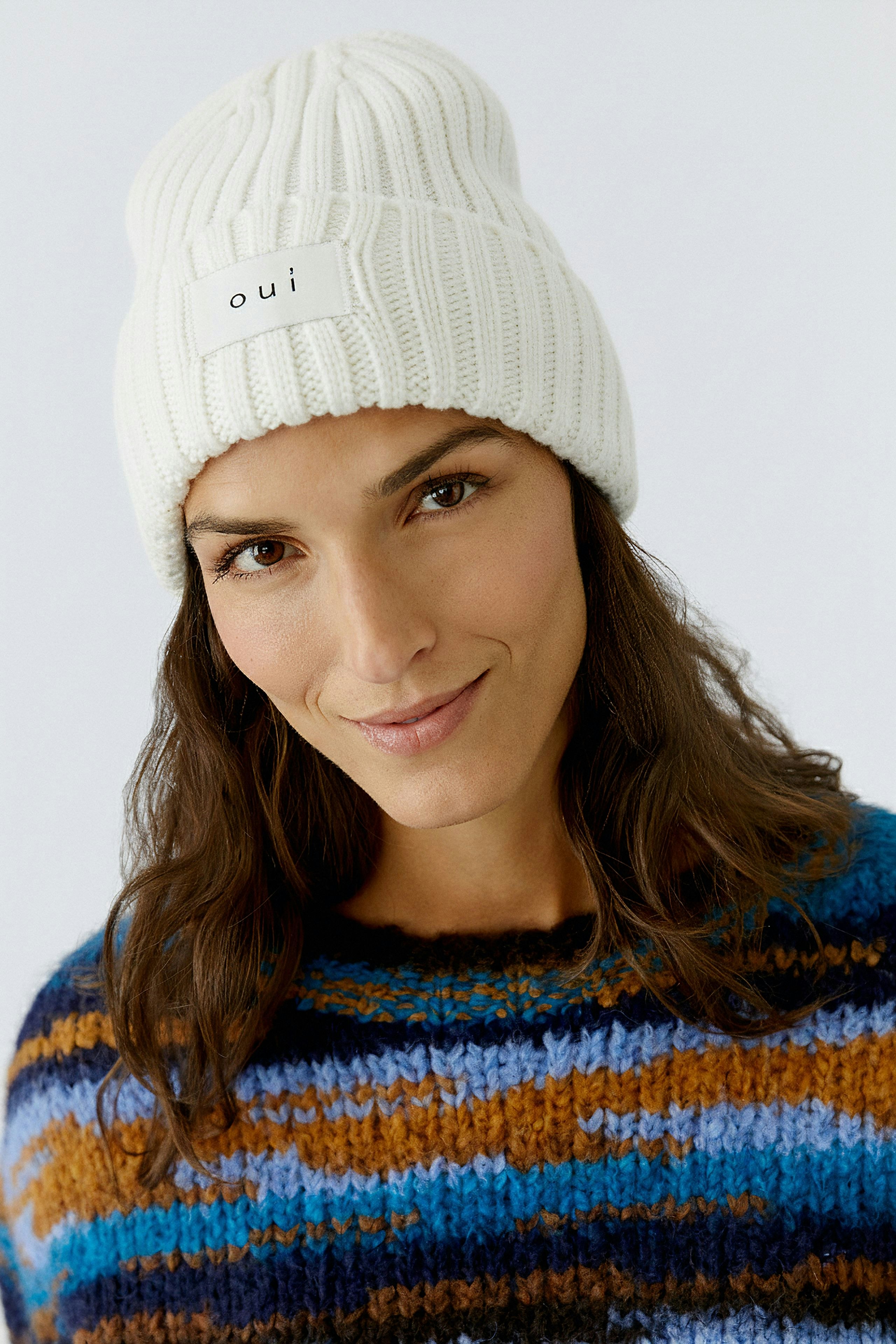 Cozy women's beanie: A woman wearing a white ribbed hat with a logo, paired with a colorful pullover.