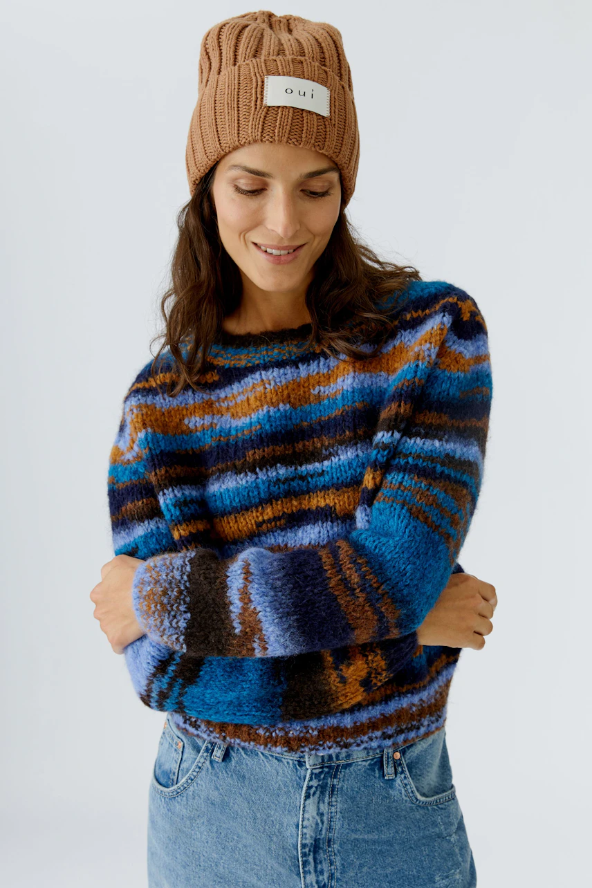 Cozy women's beanie: A woman smiles while wearing a knitted brown beanie with a logo.