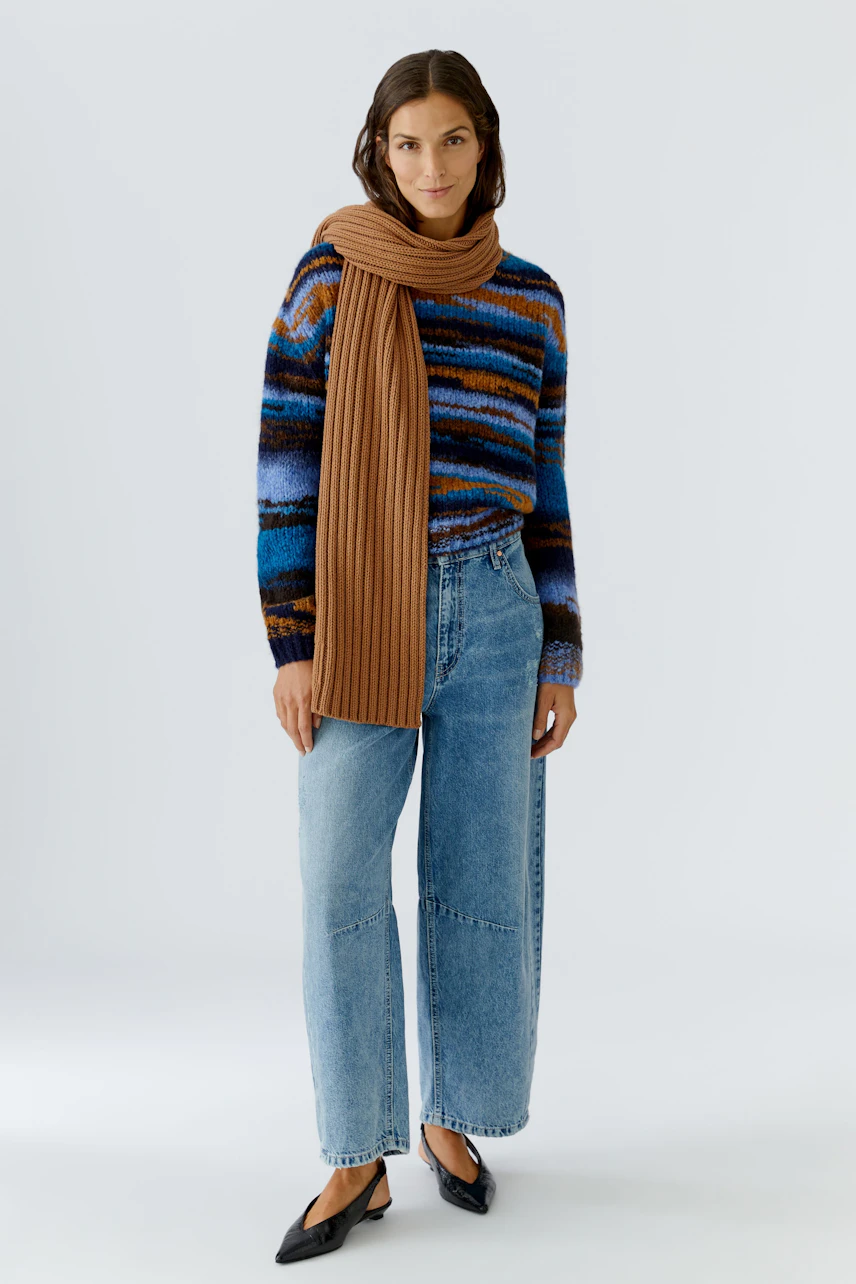 Cozy scarf worn by a woman, paired with a colorful pullover and relaxed jeans.