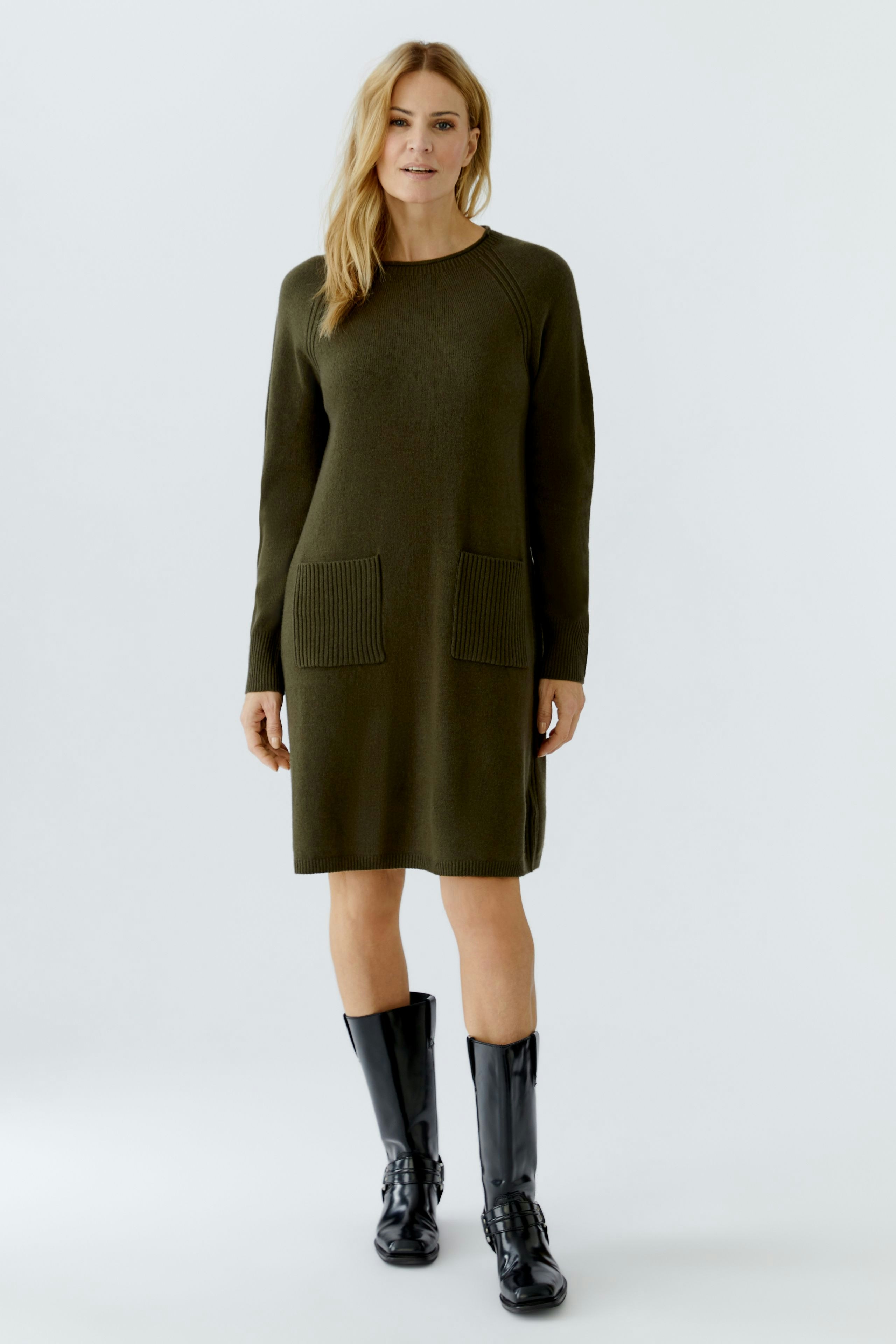 Casual women's knitted dress in olive green with two front pockets, styled with knee-high black boots.
