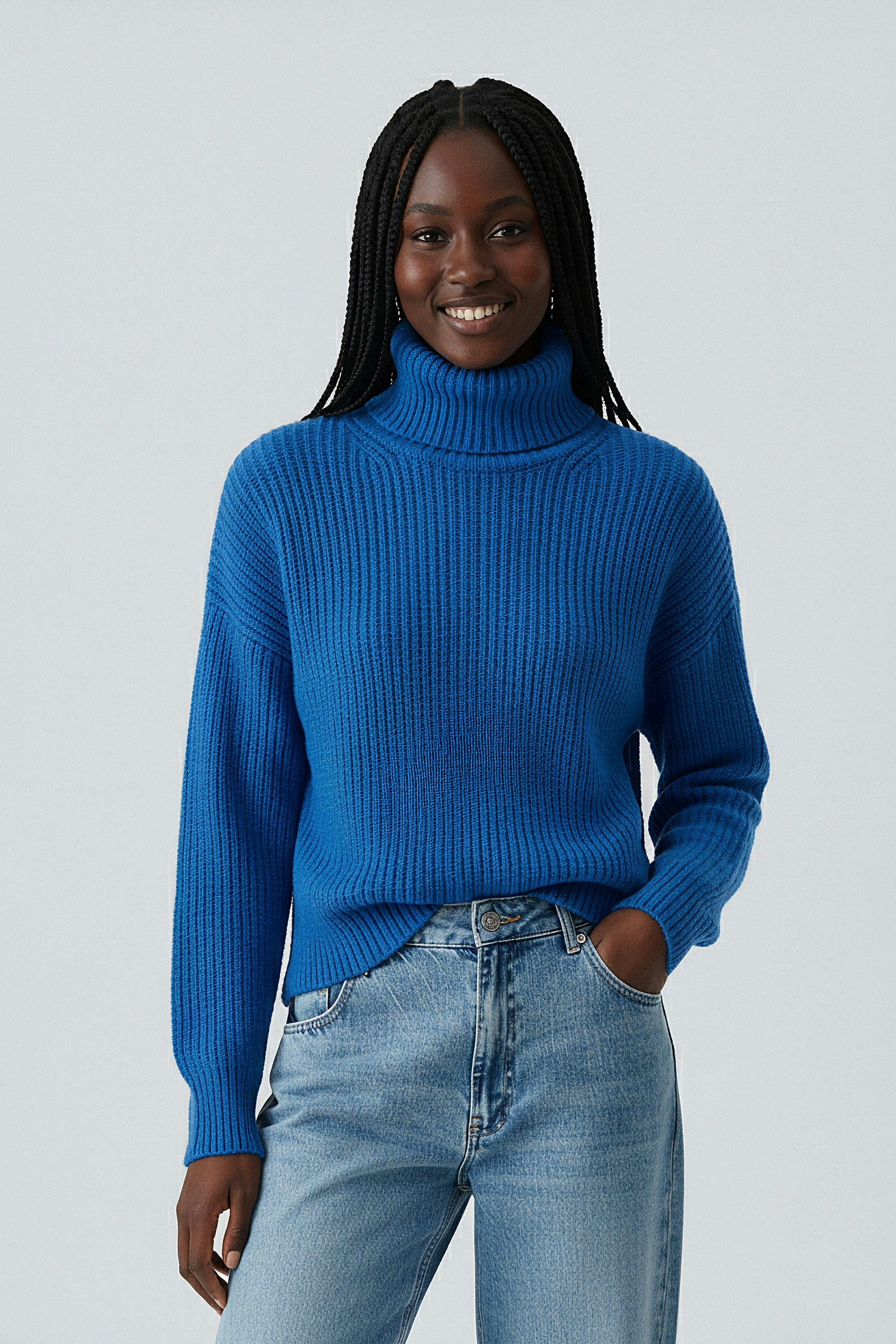 Casual women's pullover: Smiling woman in a blue turtleneck pullover paired with jeans.