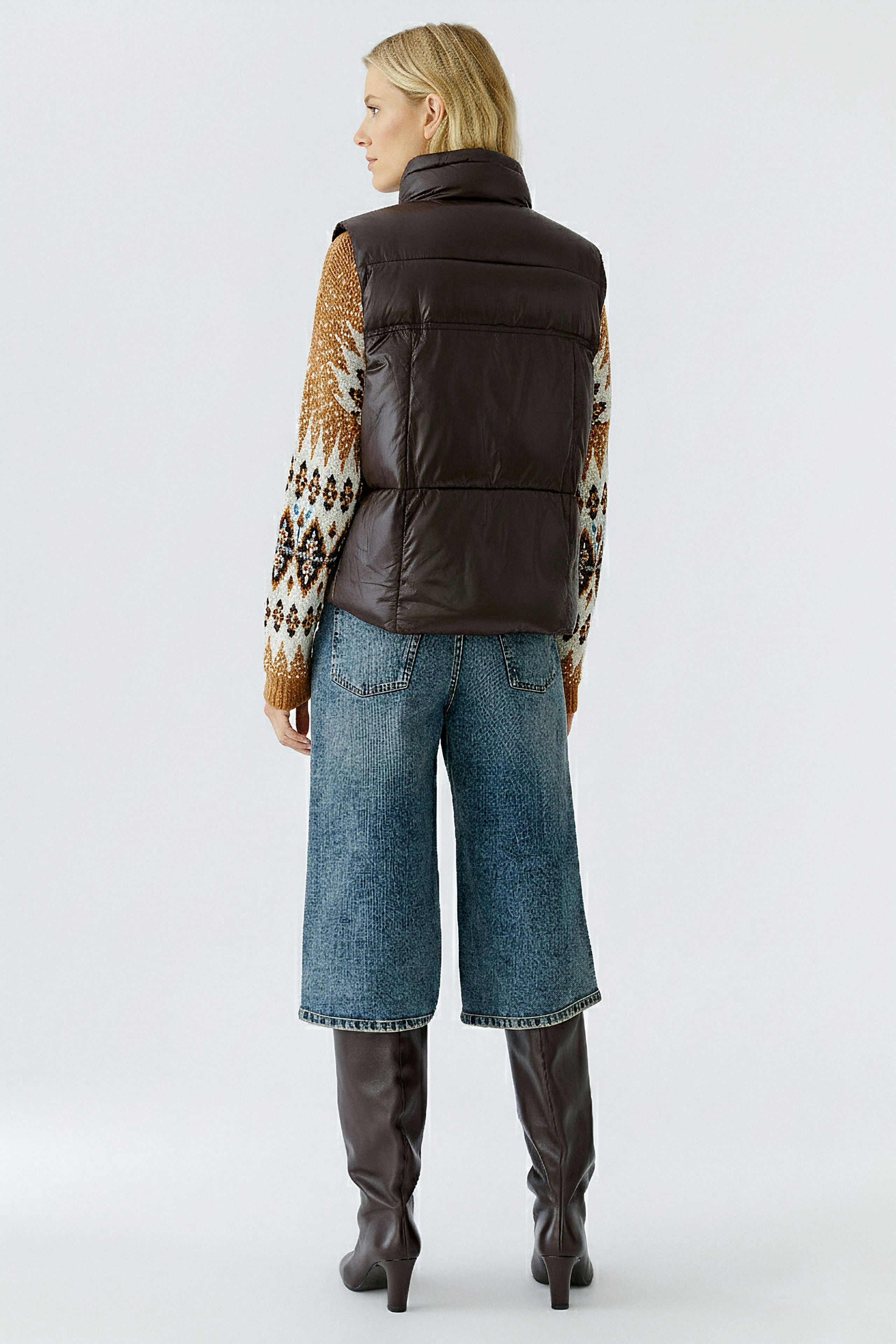 Casual women's vest: A woman in a brown padded vest over a colorful sweater, paired with denim shorts.