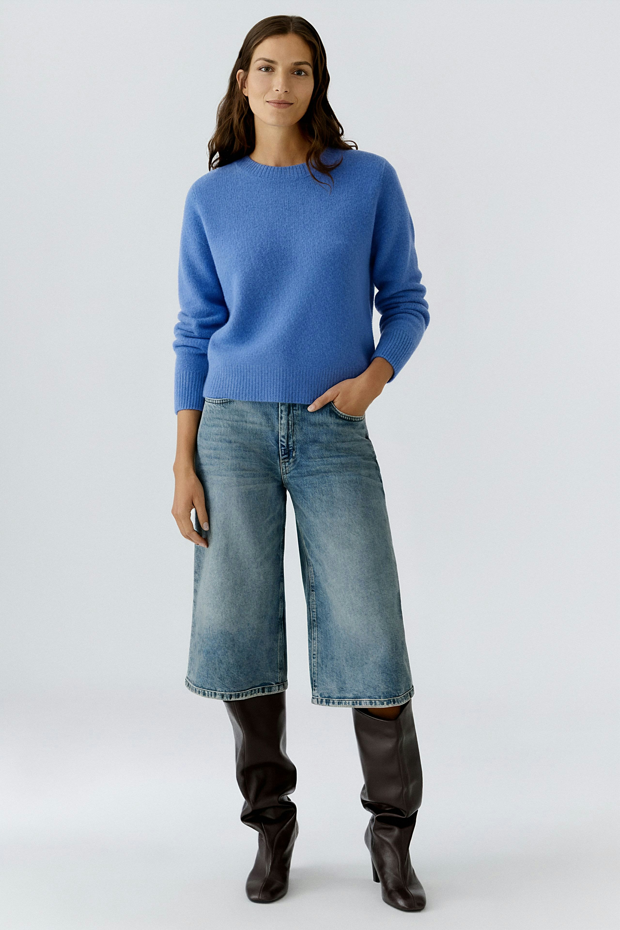 Casual women's pullover: A woman in a blue pullover paired with wide jeans and knee-high boots.