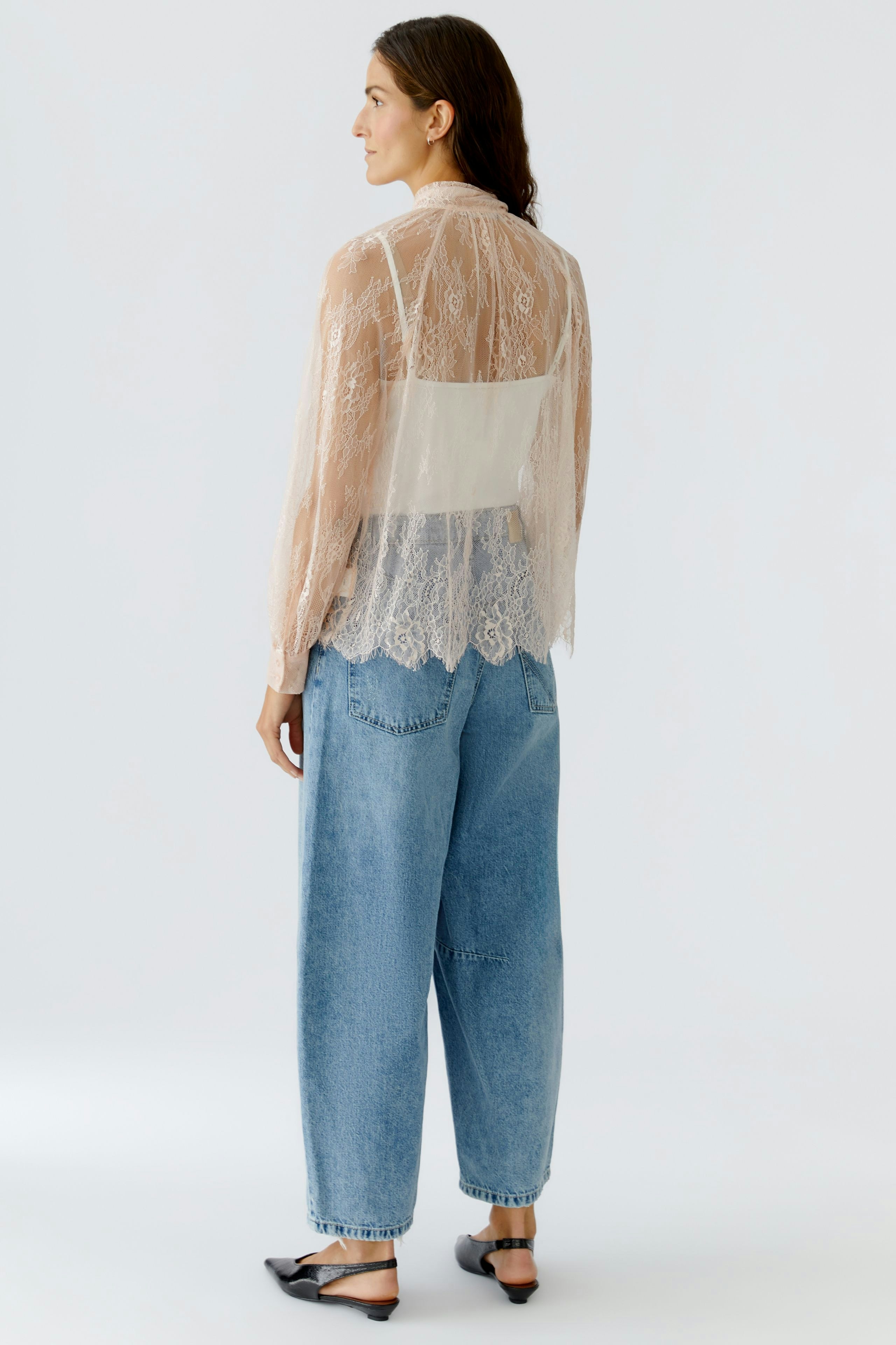 Damen-Bluse: Frau in transparenter Bluse mit Spitze und lässigen Jeans, von hinten zu sehen.