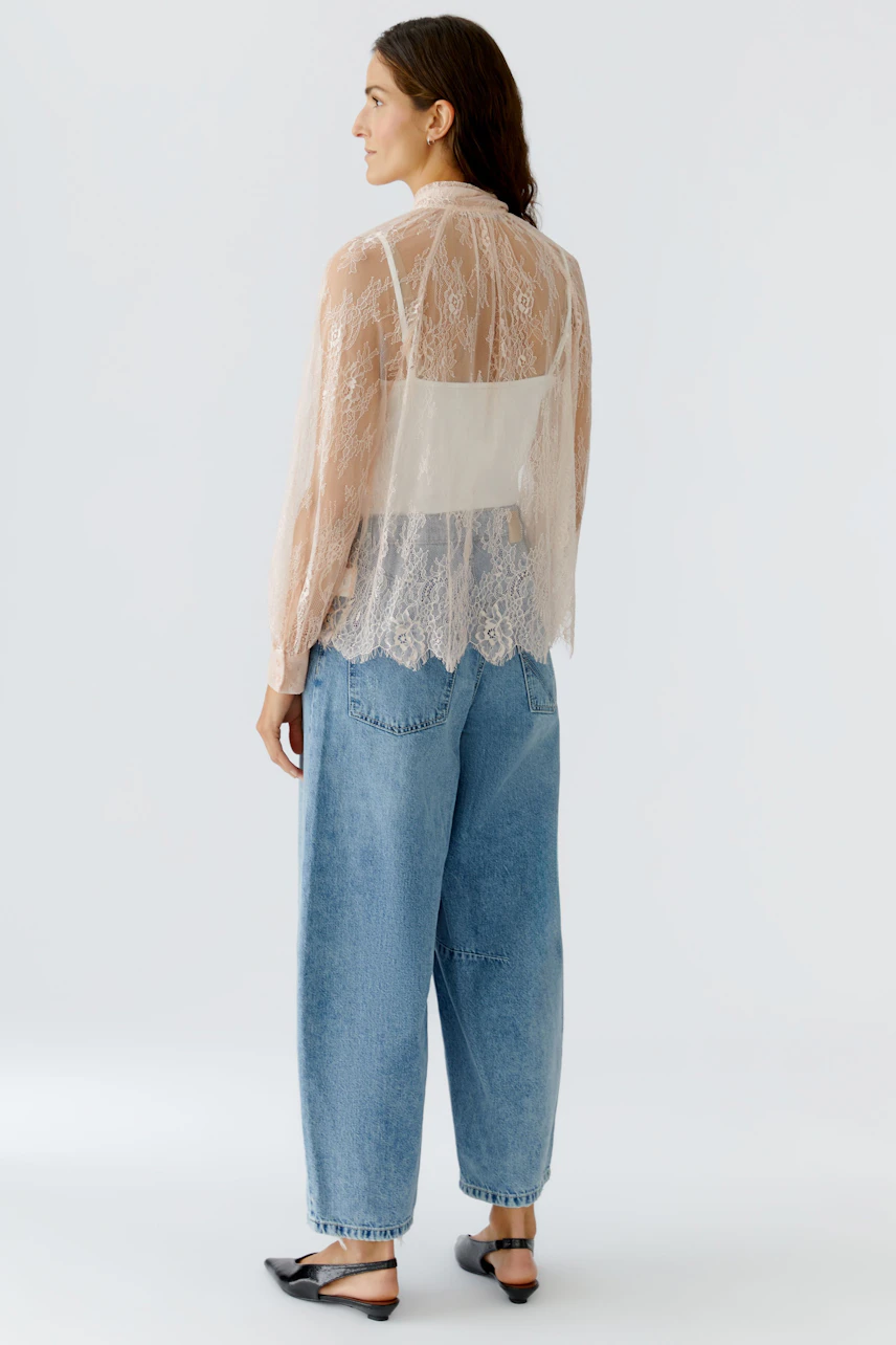 Damen-Bluse: Frau in transparenter Bluse mit Spitze und lässigen Jeans, von hinten zu sehen.
