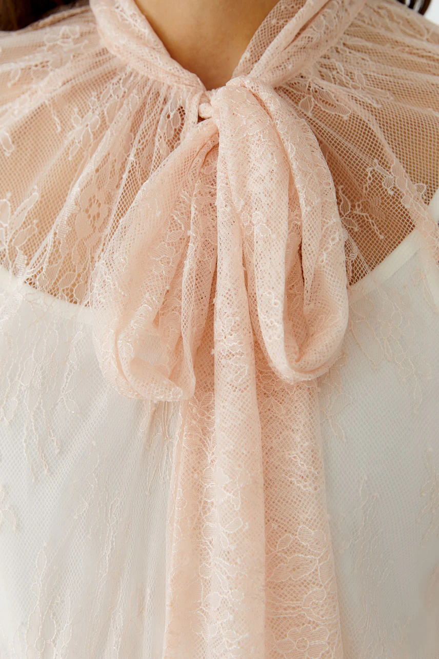 Damen-Bluse: Frau trägt eine zarte, rosa Bluse mit Spitzen-Details und einem eleganten Kragen.