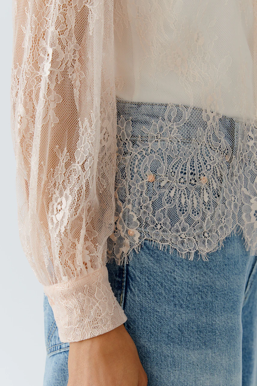 Leichte Damen-Bluse mit transparenten Ärmeln und Spitzen-Details, kombiniert mit lässigen Jeans.