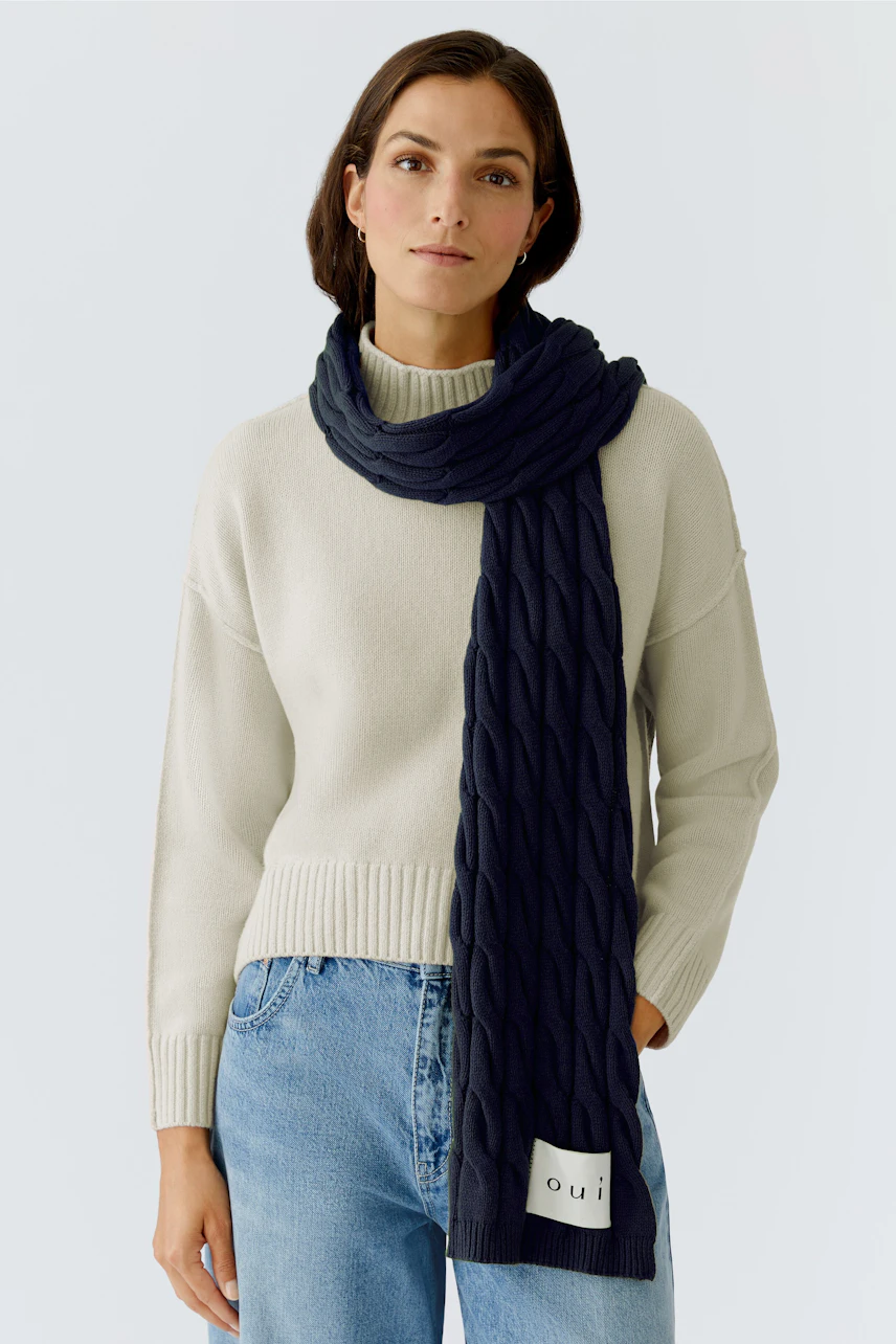 Cozy women's scarf: A woman wearing a navy knitted scarf over a light pullover, looking relaxed.