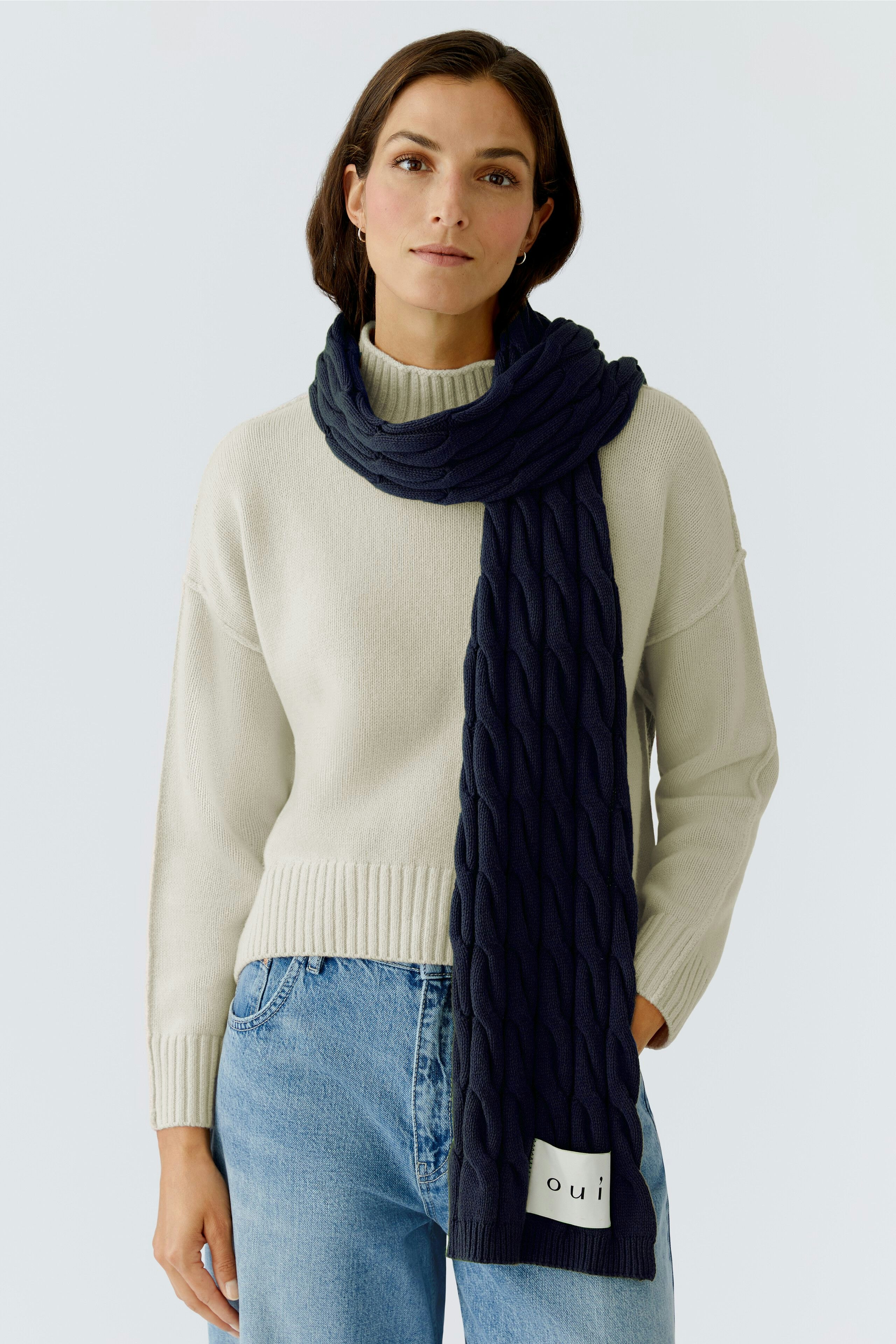 Cozy women's scarf: A woman wearing a navy knitted scarf over a light pullover, looking relaxed.