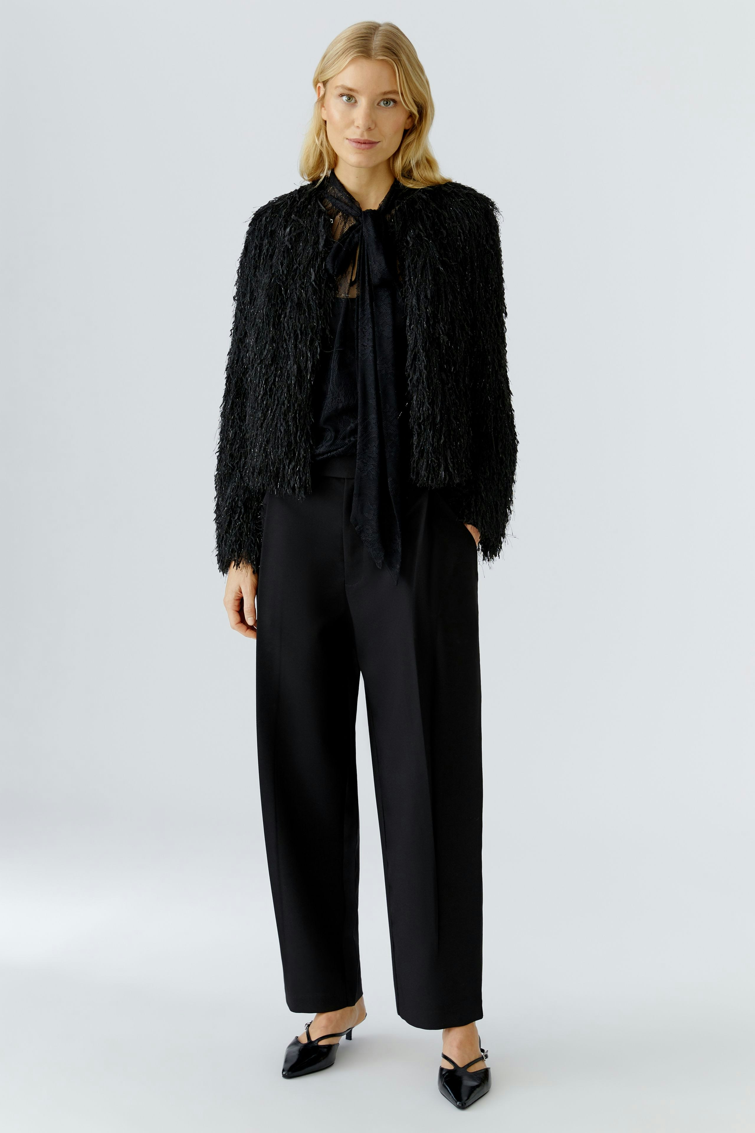 Trendy women's jacket: A woman in a black textured jacket with a tie detail, paired with loose trousers.