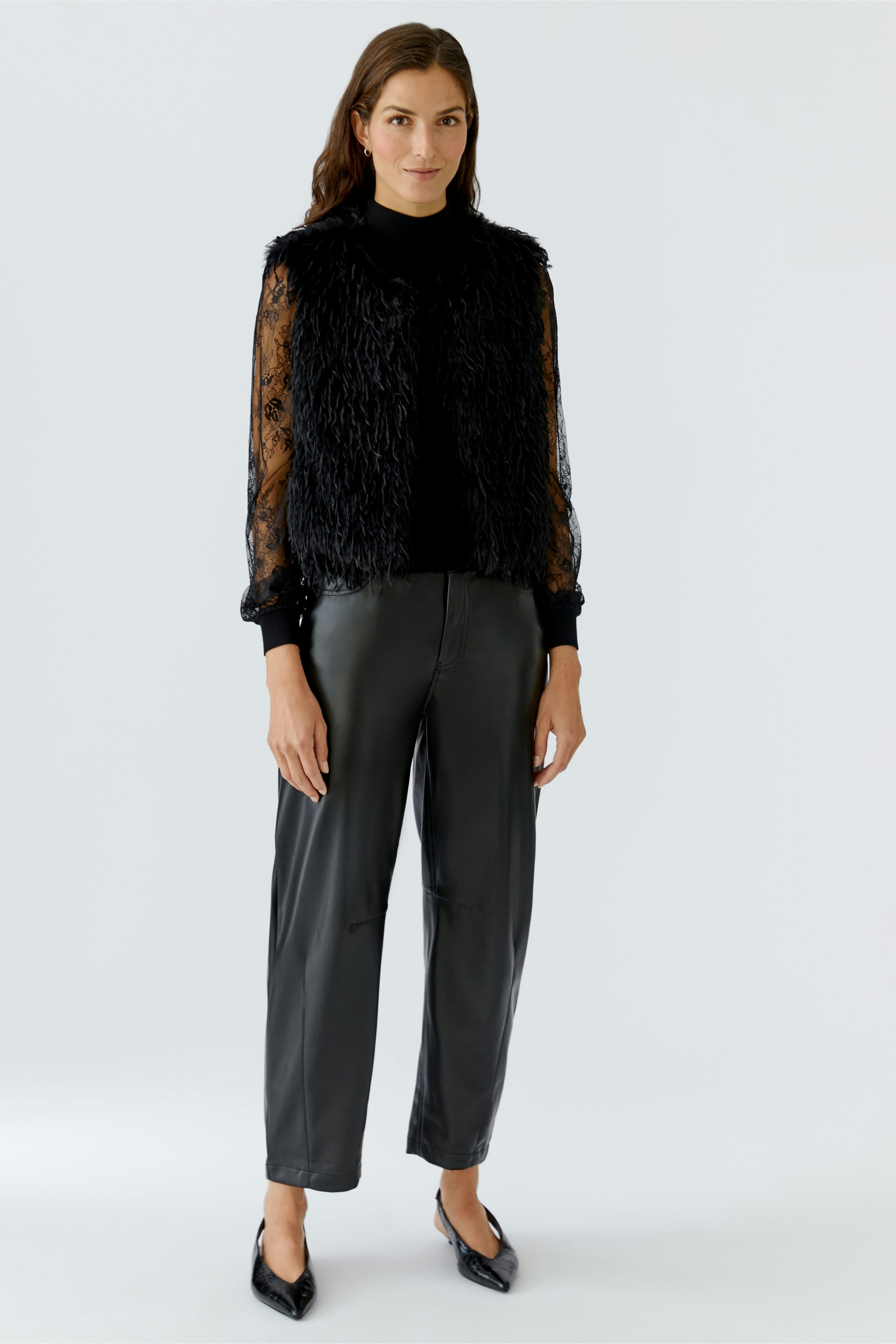 Faux fur vest: Woman in a stylish black faux fur vest over a sheer top and relaxed trousers.