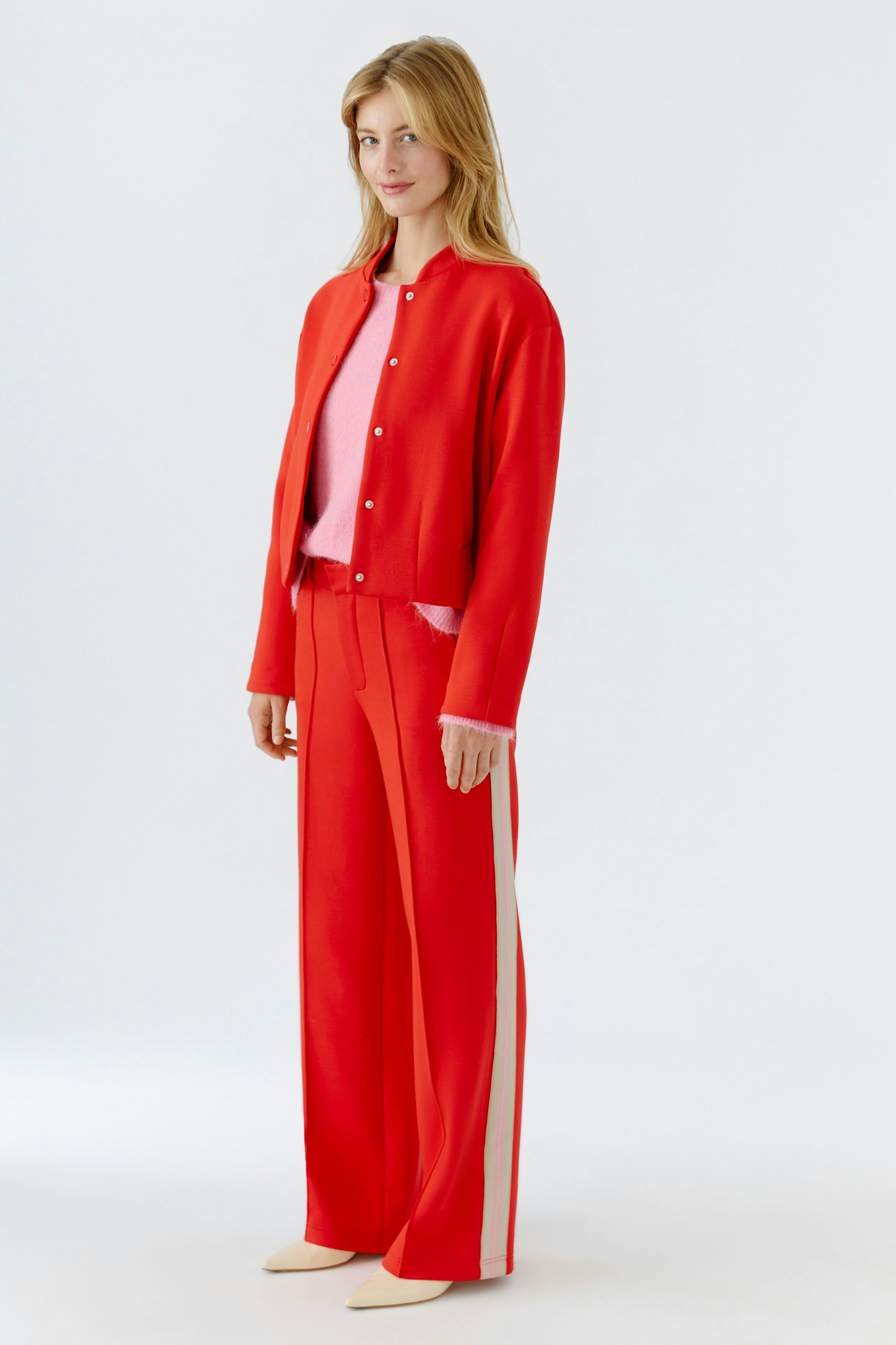 Bequeme Damen-Hose: Frau in roter Hose mit seitlichen Streifen und passendem Oberteil steht lässig.