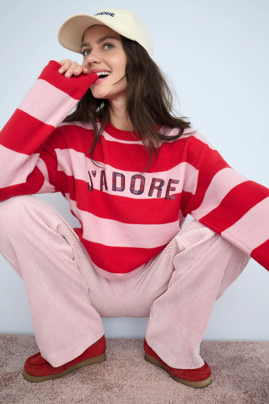 Casual women's cord pants in soft pink, paired with a striped pullover and cap.