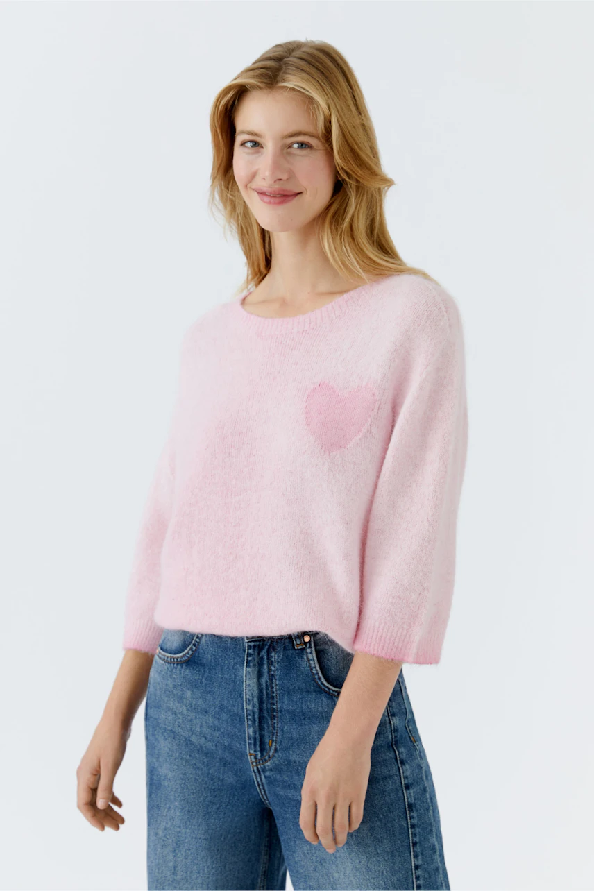 Damen-Pullover in zartem Rosa mit Herz-Applikation, lässig kombiniert mit Jeans.