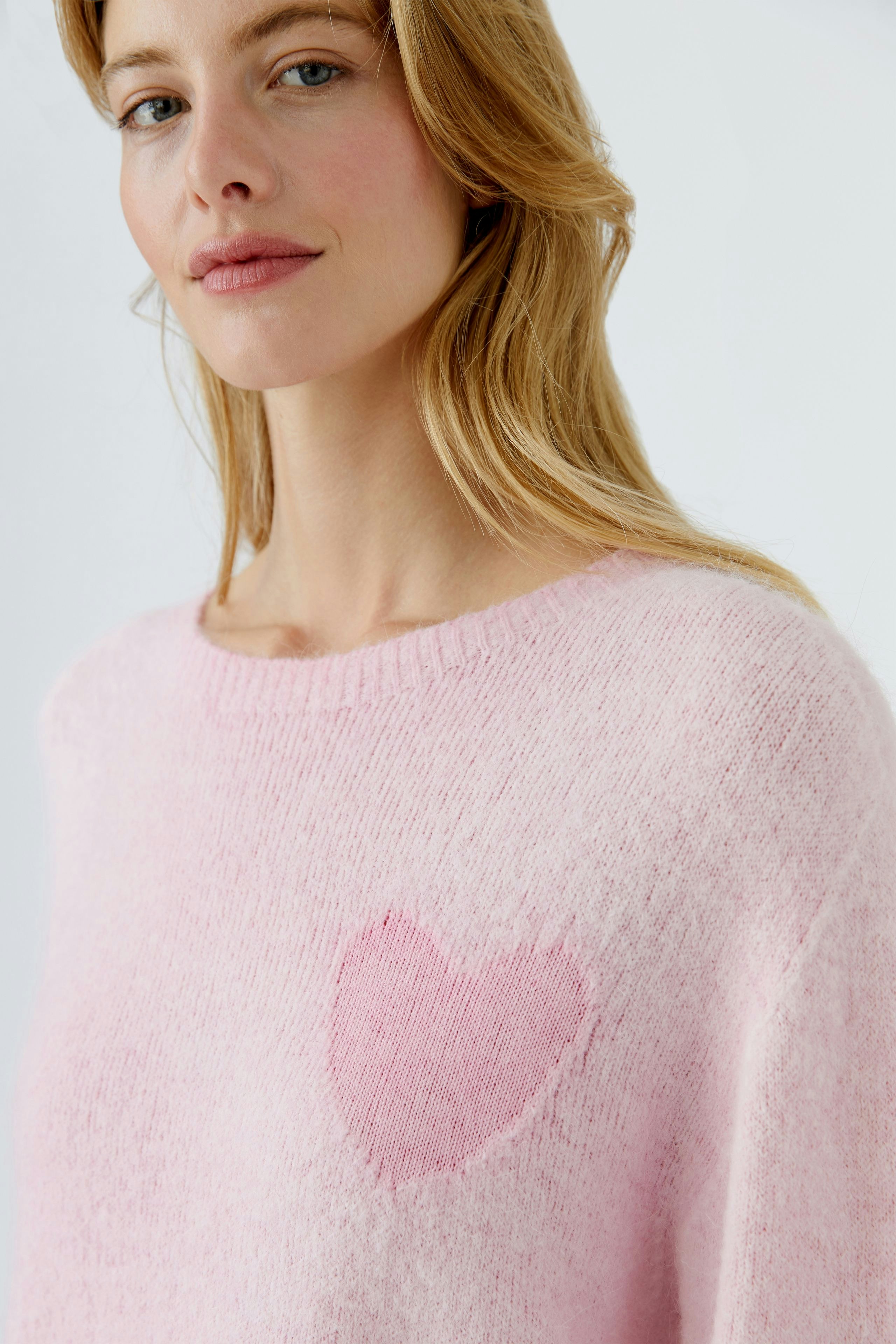 Damen-Pullover in zartem Rosa mit Herzmotiv. Junge Frau trägt den kuscheligen Pullover.