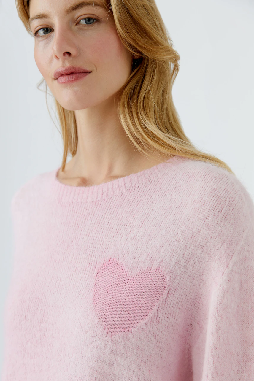 Damen-Pullover in zartem Rosa mit Herzmotiv. Junge Frau trägt den kuscheligen Pullover.