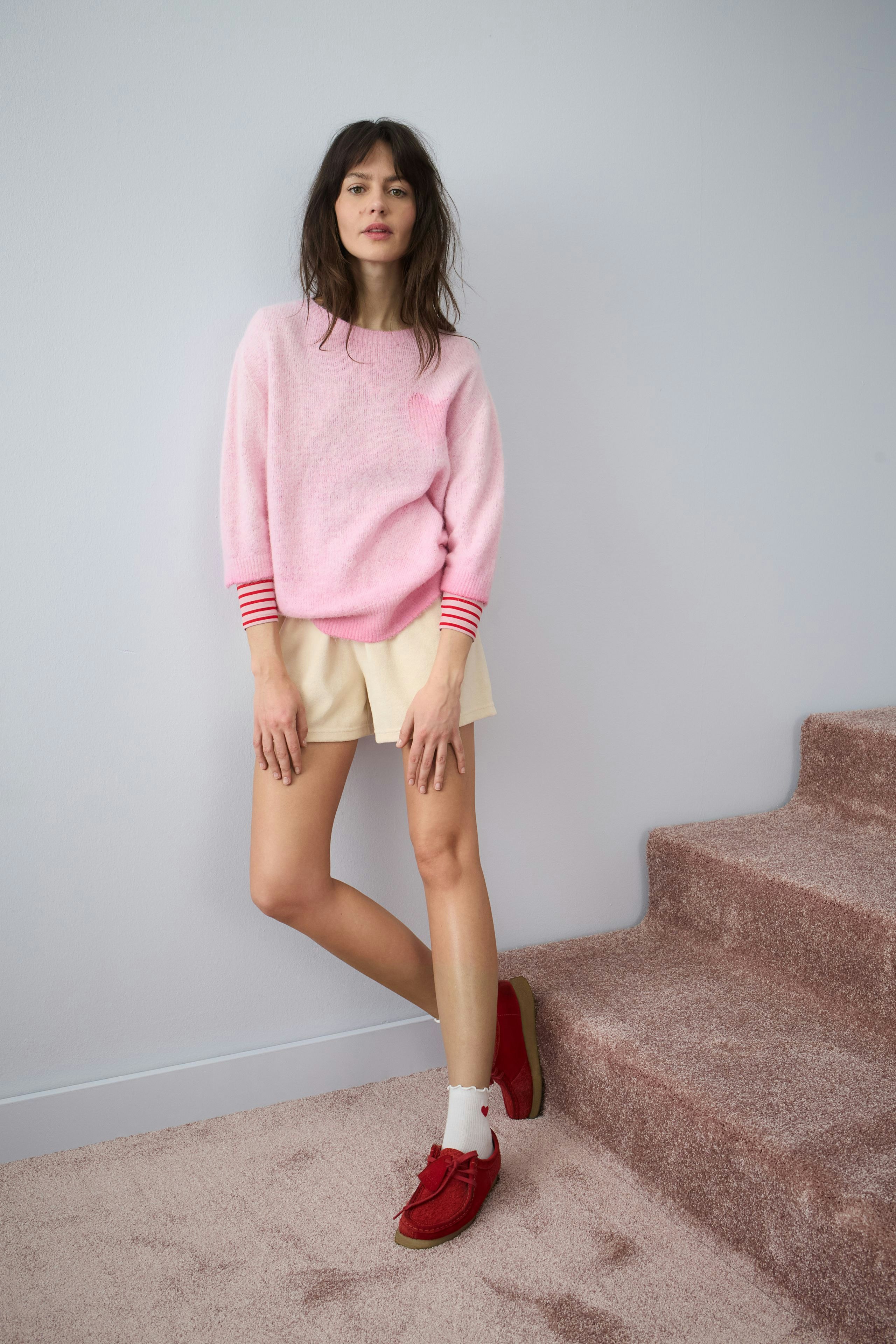 Damen-Pullover in Pink mit gestreiften Ärmeln, kombiniert mit Shorts und lässigen Schuhen.
