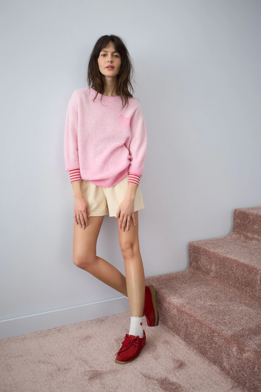 Damen-Pullover in Pink mit gestreiften Ärmeln, kombiniert mit Shorts und lässigen Schuhen.