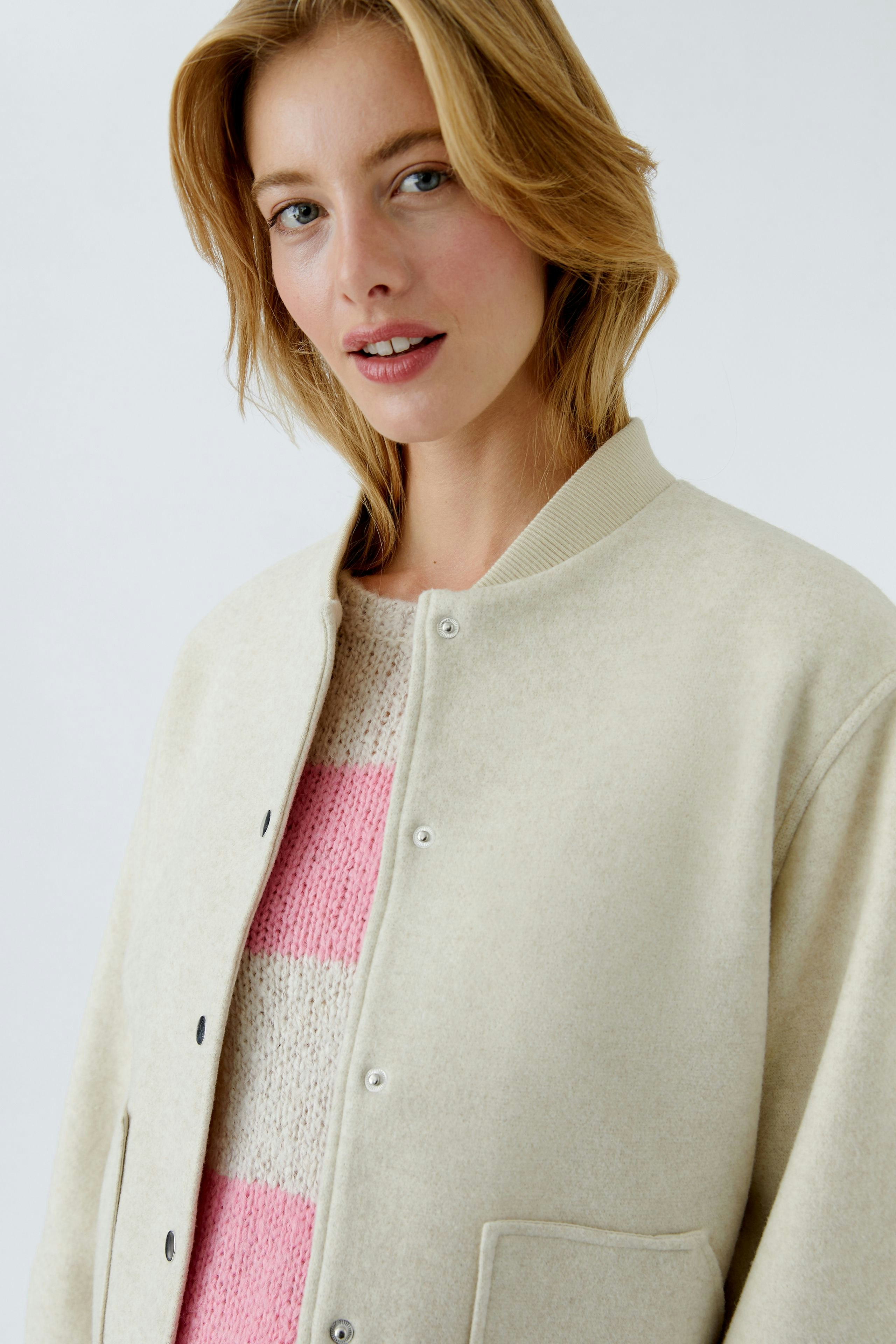 Casual women's blouson: Young woman in a cream bomber jacket over a pink striped pullover, smiling.