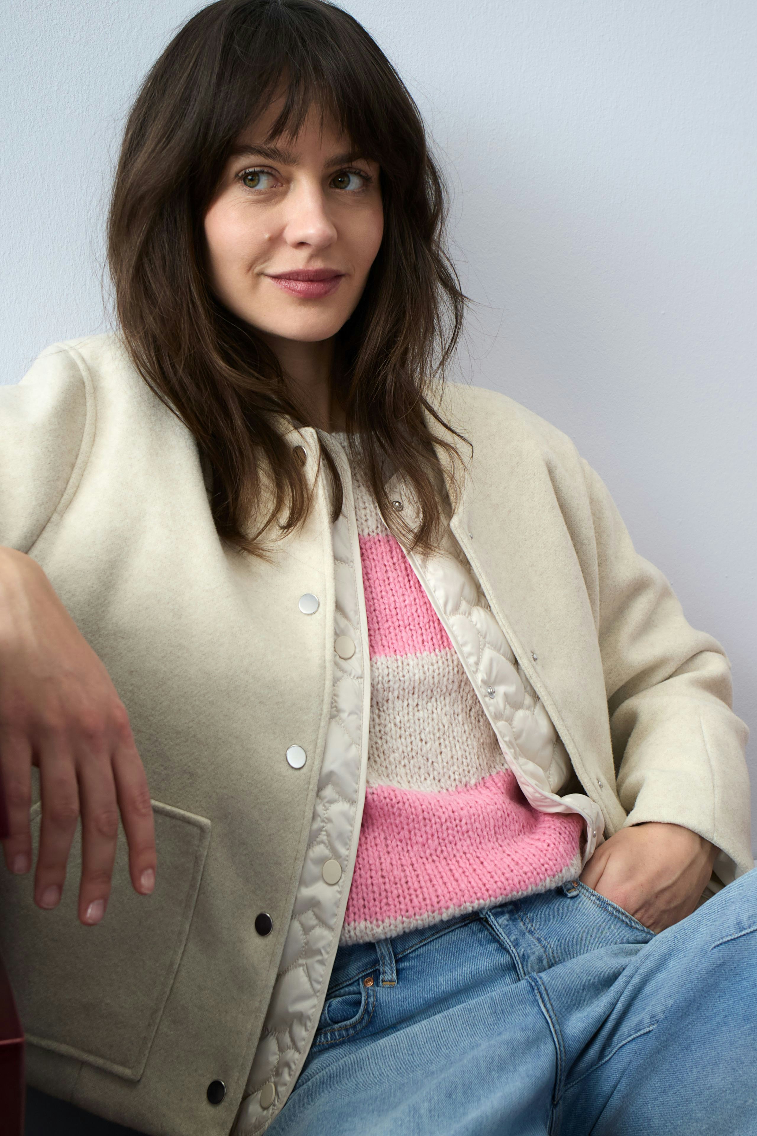 Casual women's blouson: Woman in a light jacket over a pink and white pullover, relaxed pose.