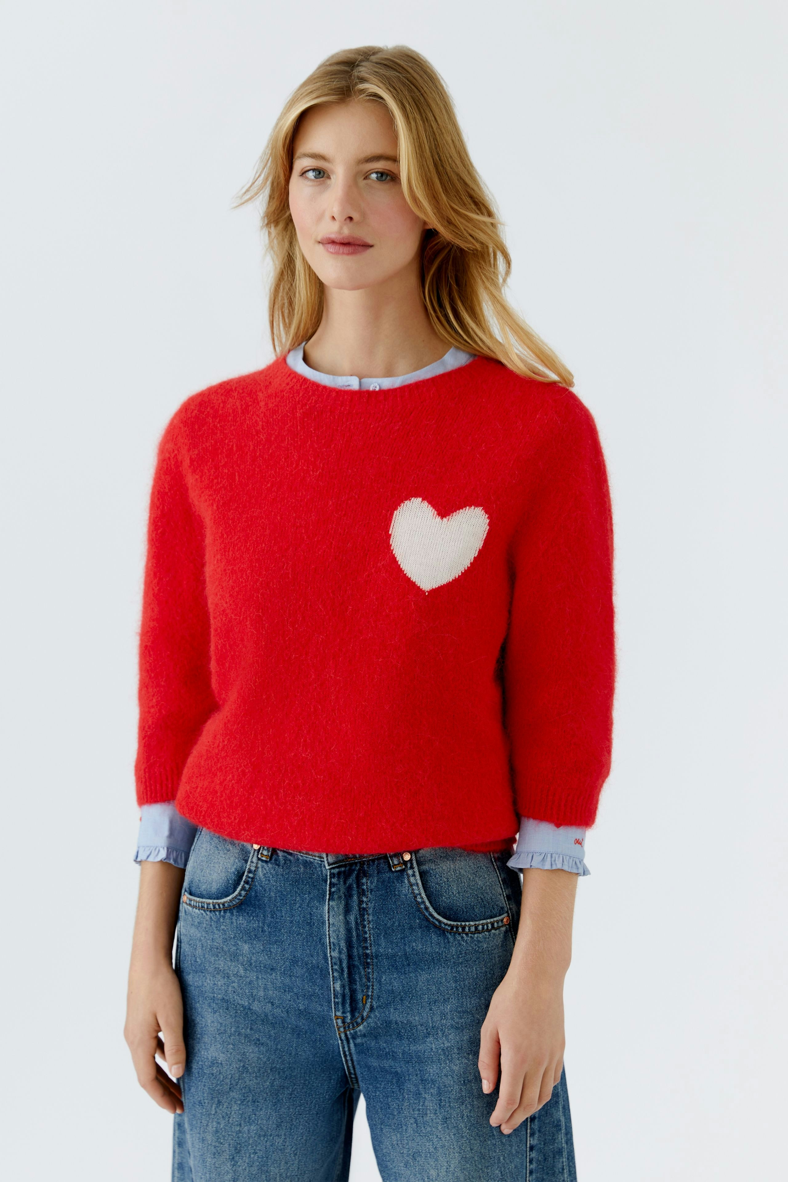 Roter Damen-Pullover mit Herzmotiv, lässig kombiniert mit Jeans und blauer Bluse.