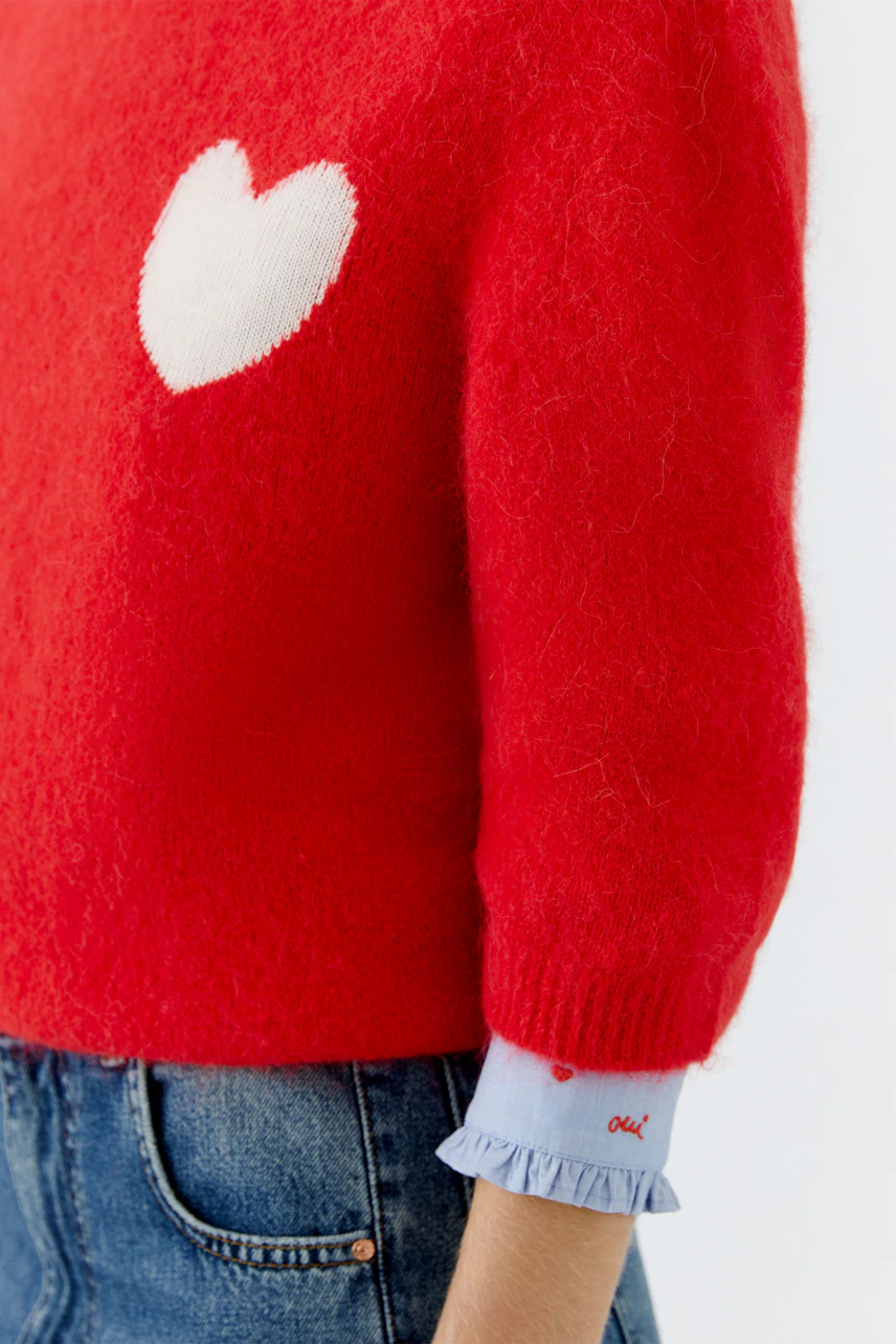 Casual women's pullover: A red knit pullover with a white heart detail, paired with denim.