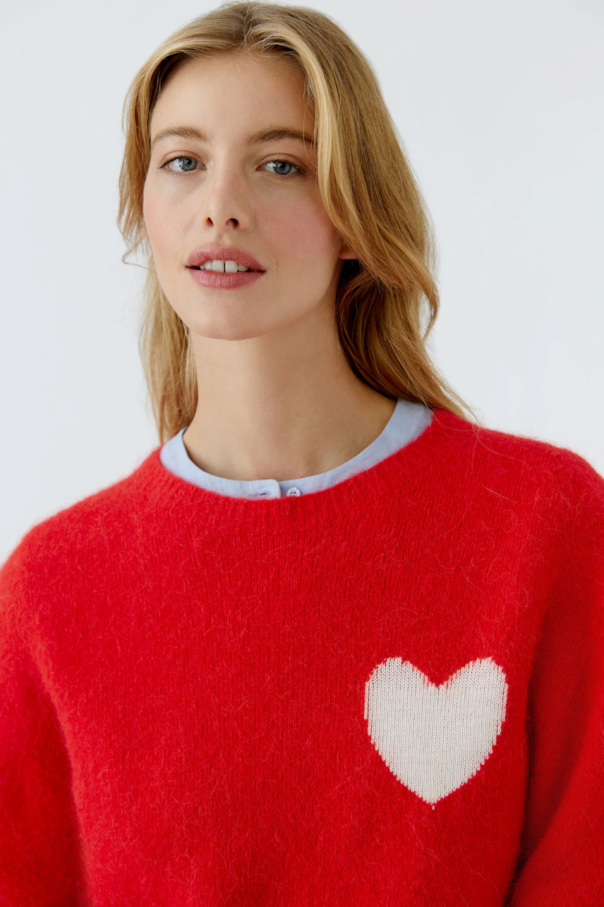 Casual women's pullover: A woman in a red sweater with a heart design, paired with a light blue collar.