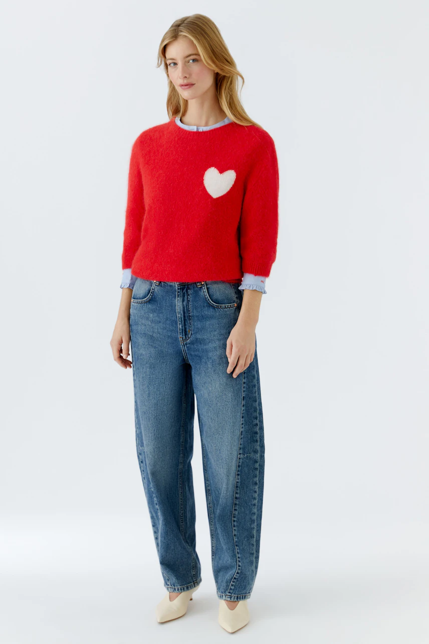 Casual women's pullover: Young woman in a red fluffy pullover with a heart design, paired with relaxed jeans.