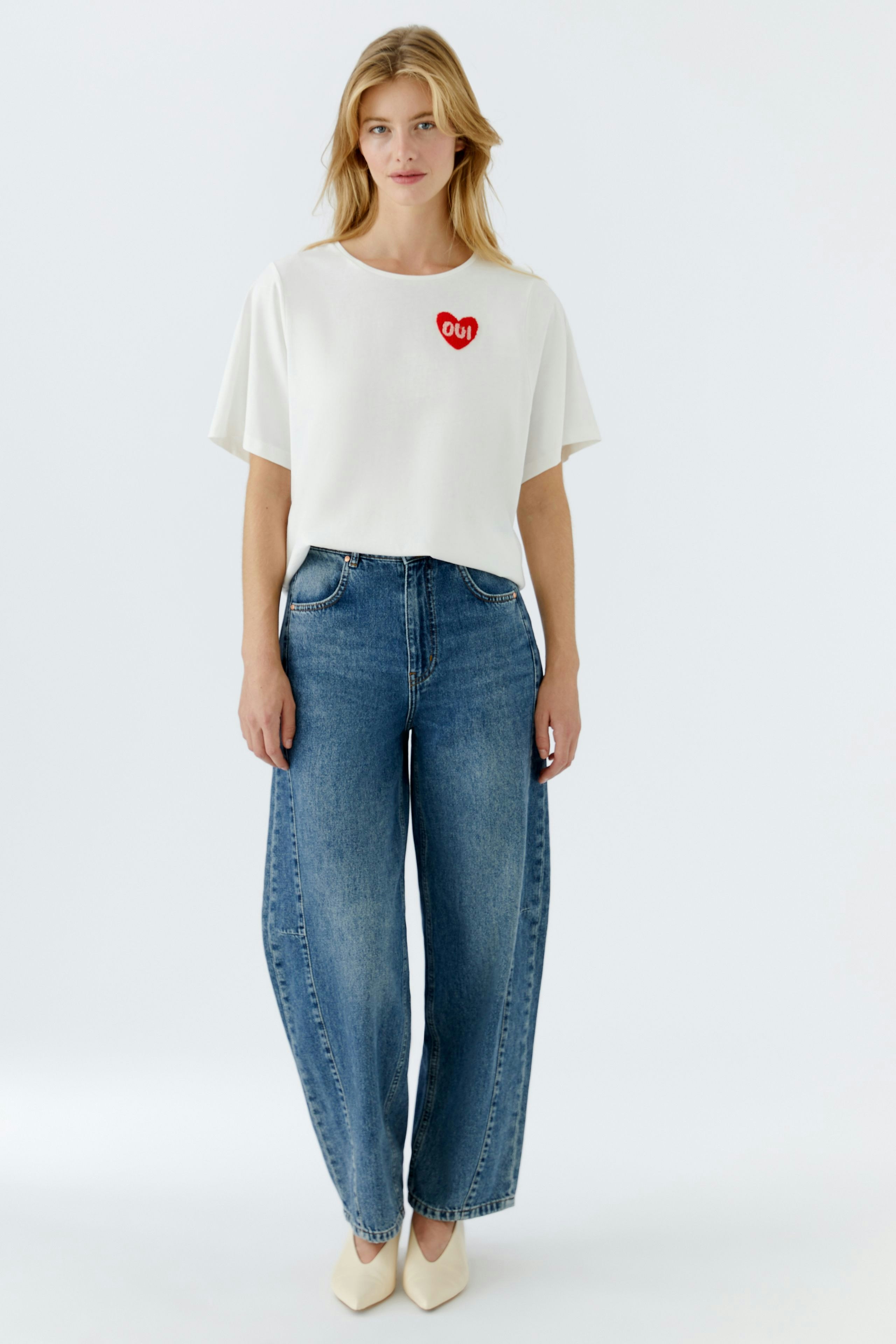 Casual women's T-shirt: Young woman in a white tee with a heart design, paired with relaxed jeans.