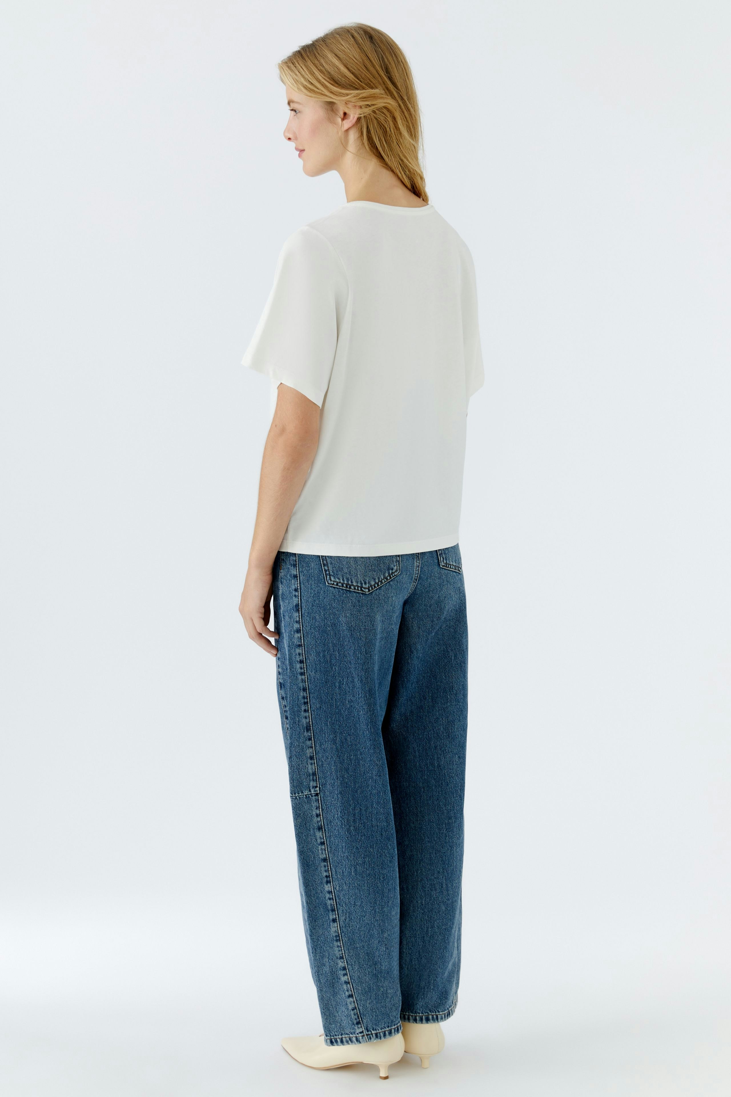 Casual women's T-shirt: Young woman in a white top paired with relaxed-fit jeans.