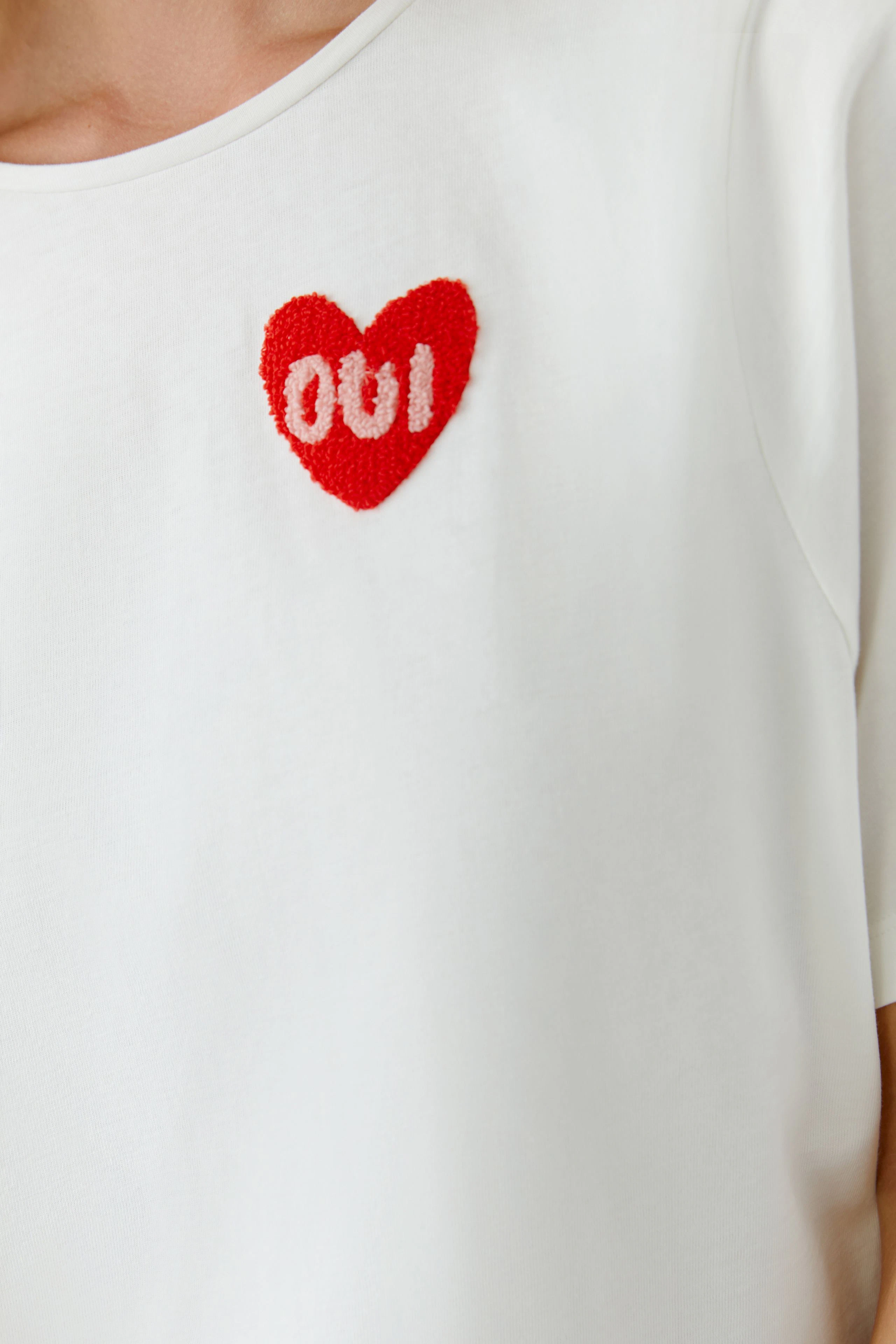 Casual women's T-shirt: Close-up of a woman in a white tee with a red heart and 'oui' design.