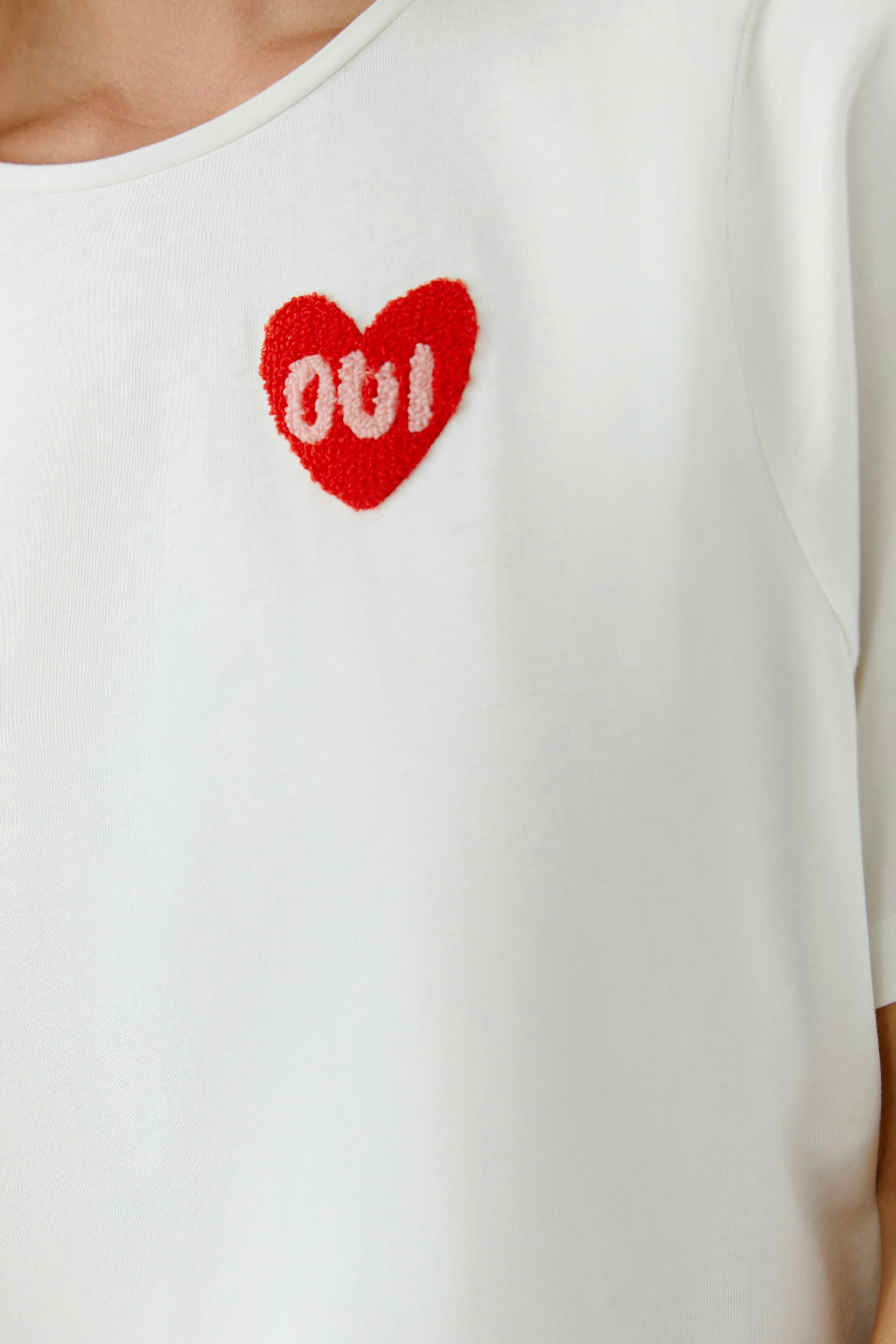 Casual women's T-shirt: Close-up of a woman in a white tee with a red heart and 'oui' design.