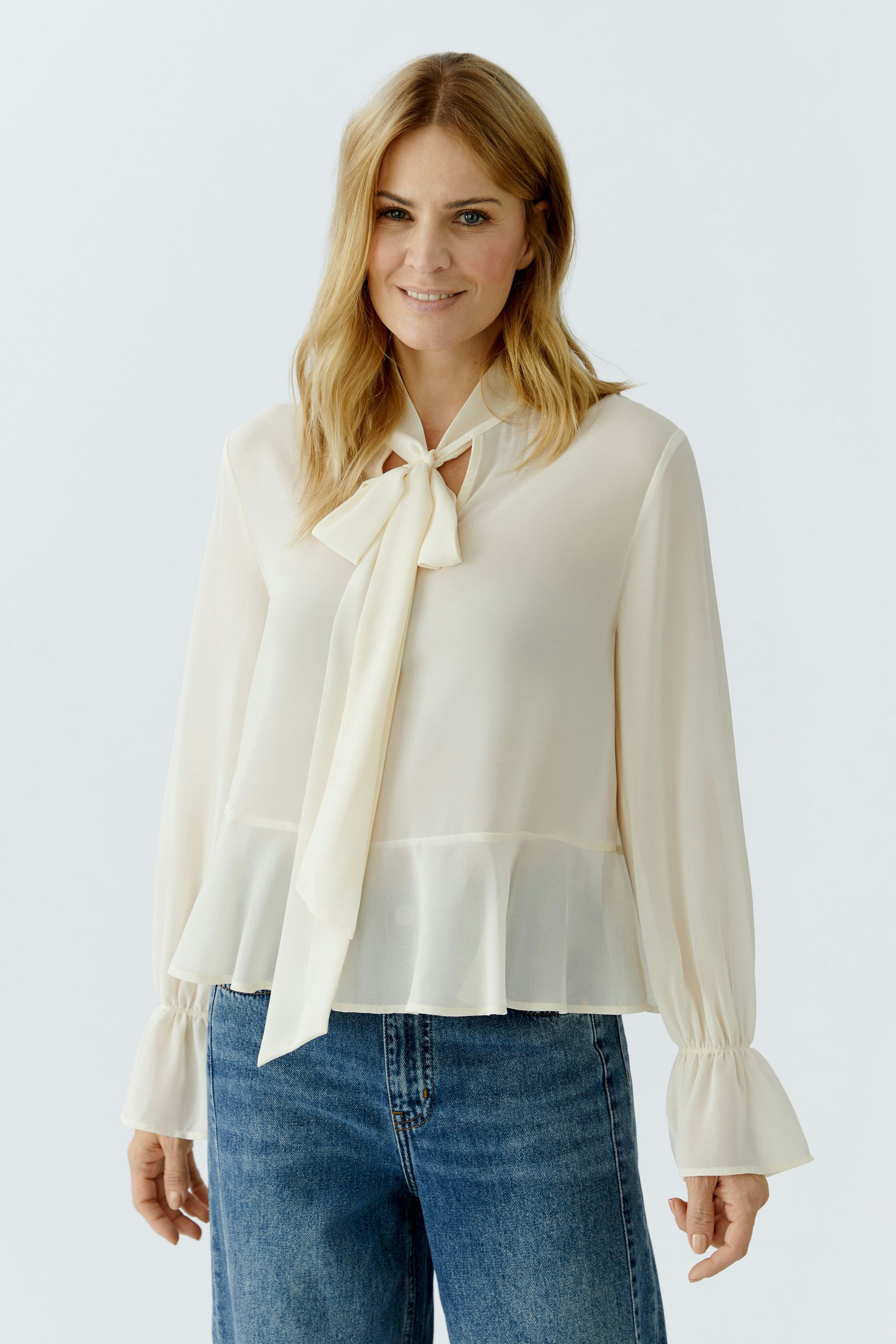 Light blouse with a tie detail: Woman wearing a cream blouse with flared sleeves and a peplum hem.