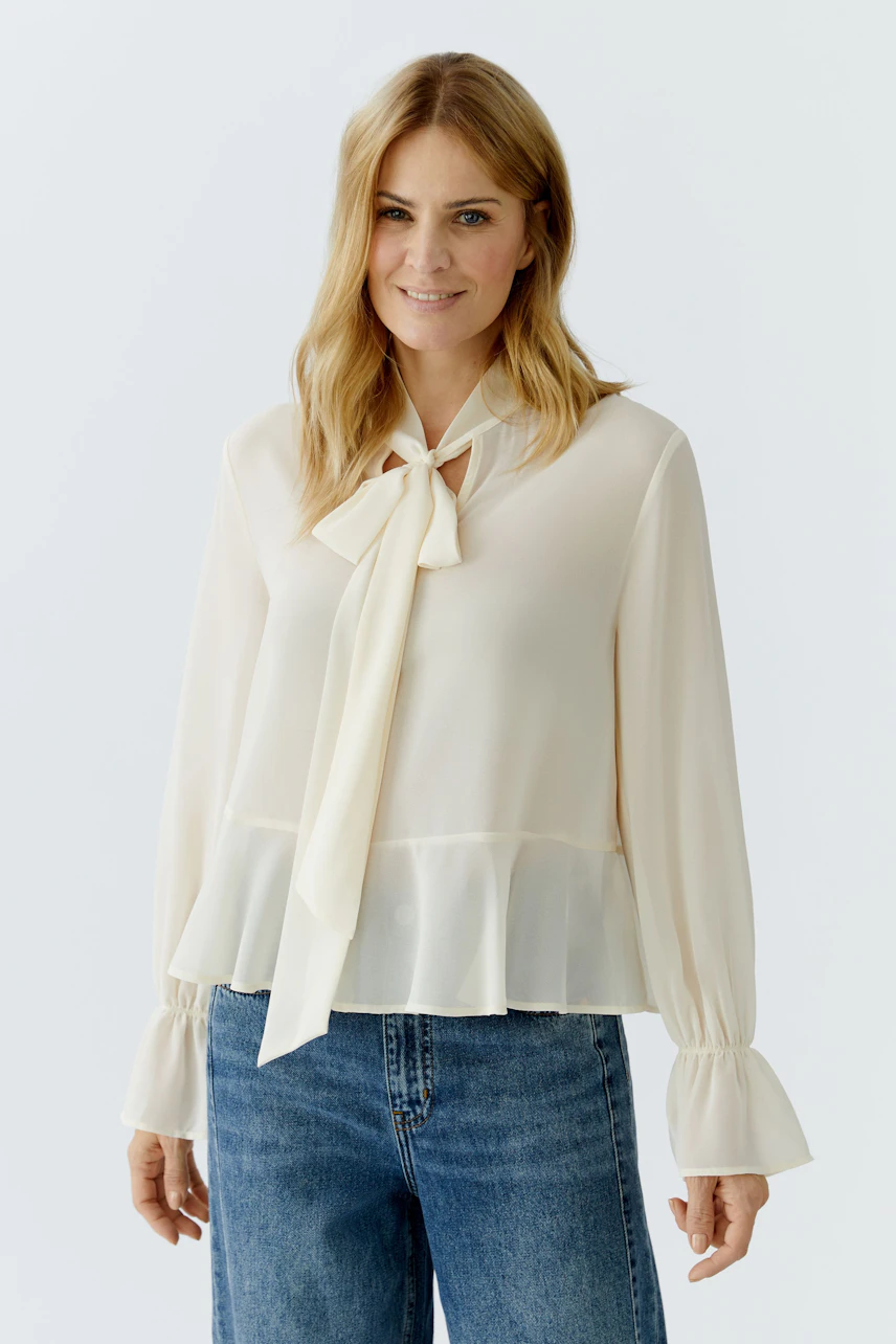 Light blouse with a tie detail: Woman wearing a cream blouse with flared sleeves and a peplum hem.
