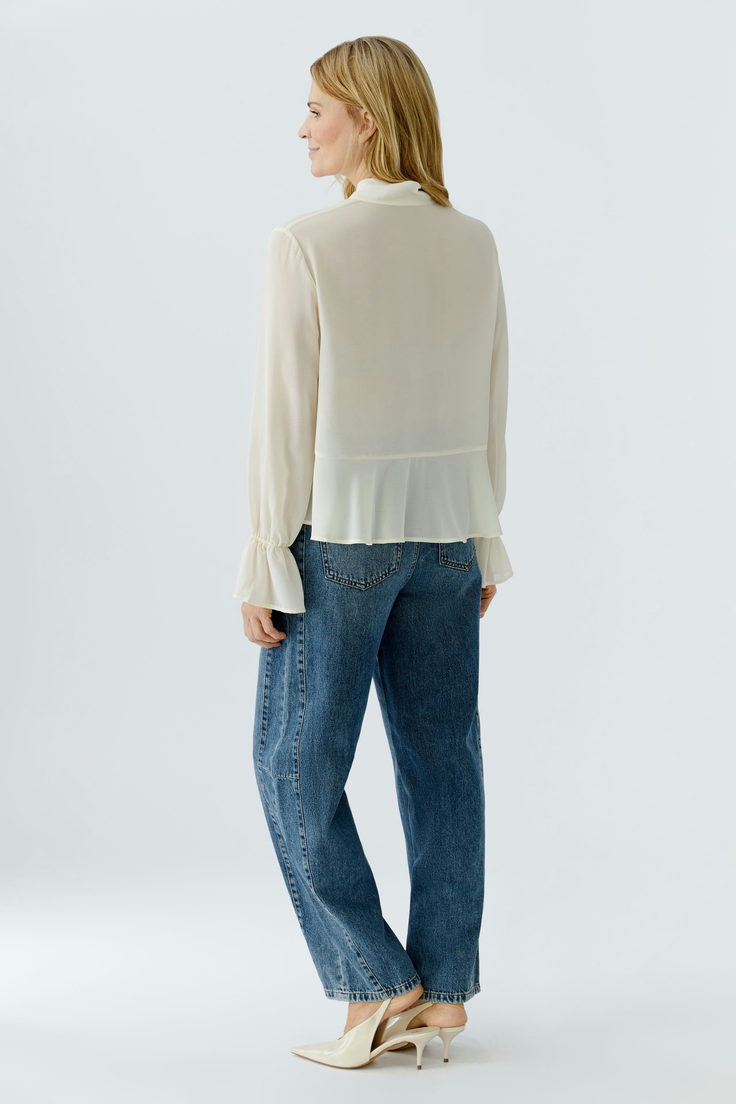 Lightweight blouse: Woman in a flowing cream blouse with ruffled sleeves and relaxed jeans.