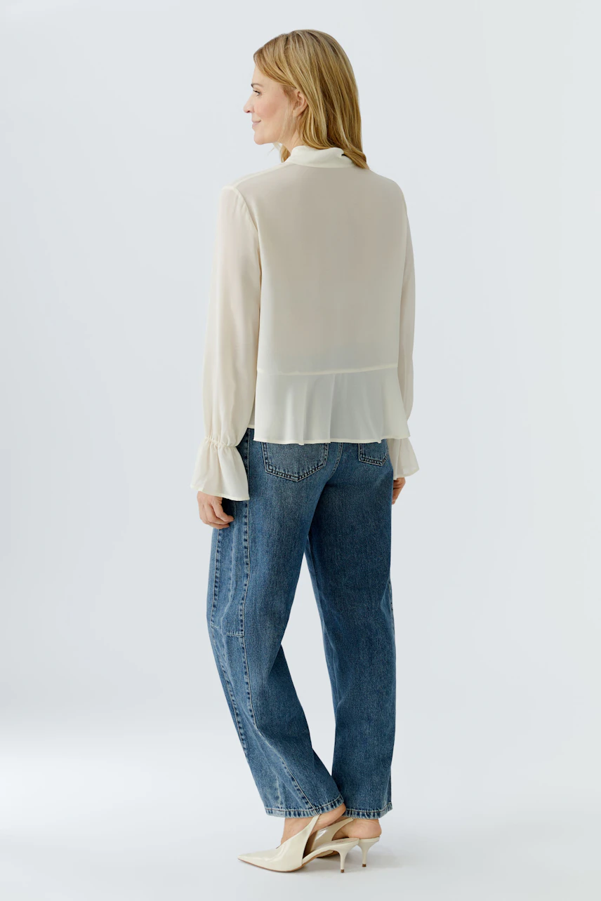 Lightweight blouse: Woman in a flowing cream blouse with ruffled sleeves and relaxed jeans.