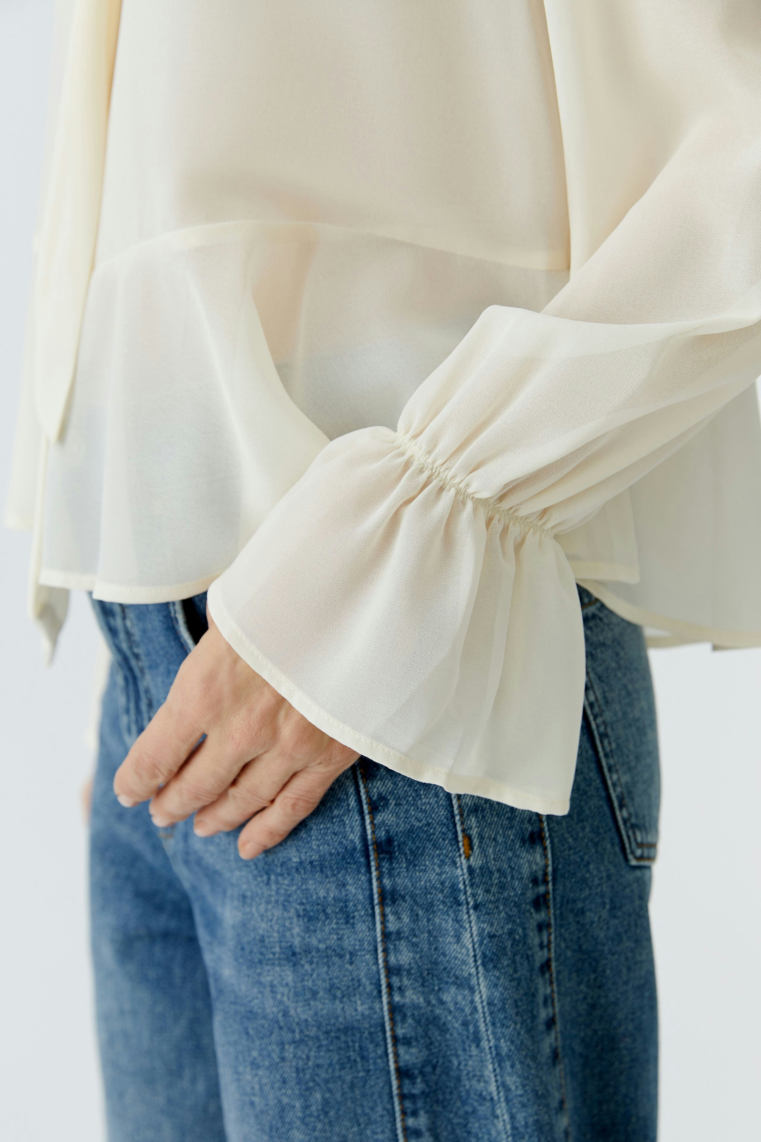 Light blouse: Woman in a flowing cream blouse with gathered sleeves, paired with casual jeans.