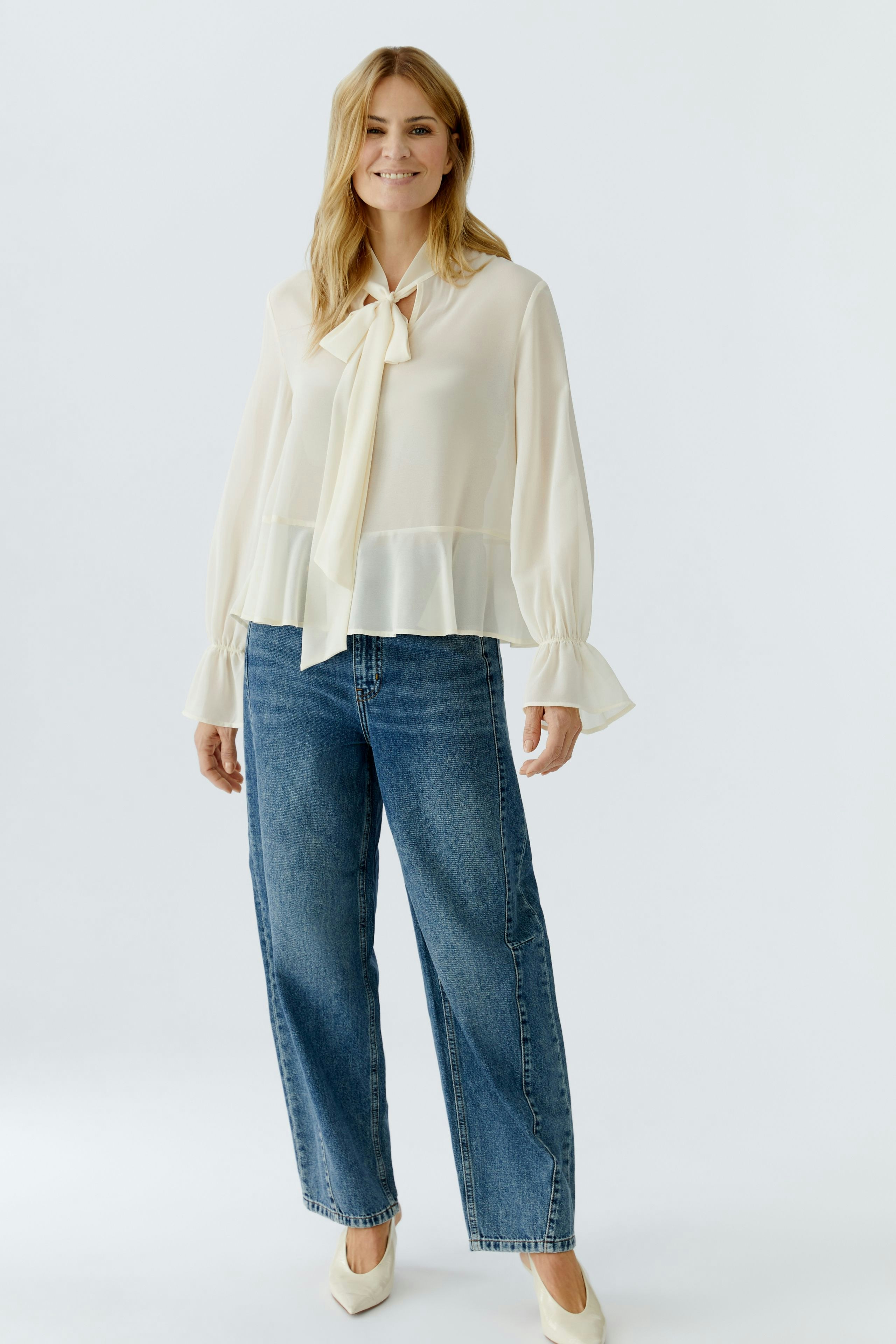 Light blouse: Woman in a cream blouse with a tie detail, paired with relaxed-fit jeans.