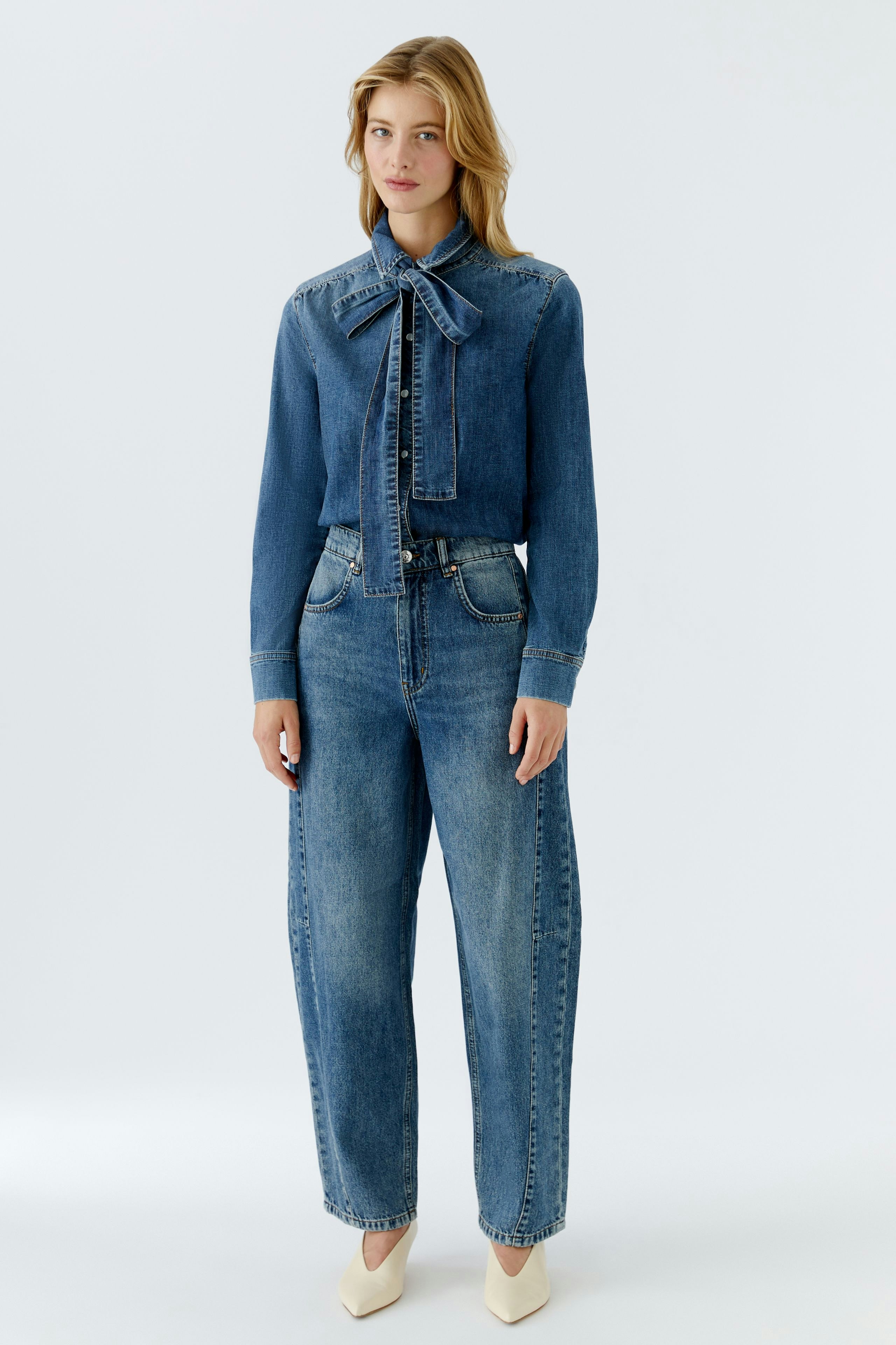 Casual women's denim shirt: A woman in a blue denim shirt with a bow tie and relaxed fit jeans.