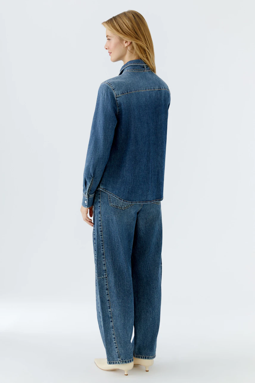 Damen-Jeanshemd: Frau trägt ein lässiges, blaues Jeanshemd mit langen Ärmeln und lockerer Passform.