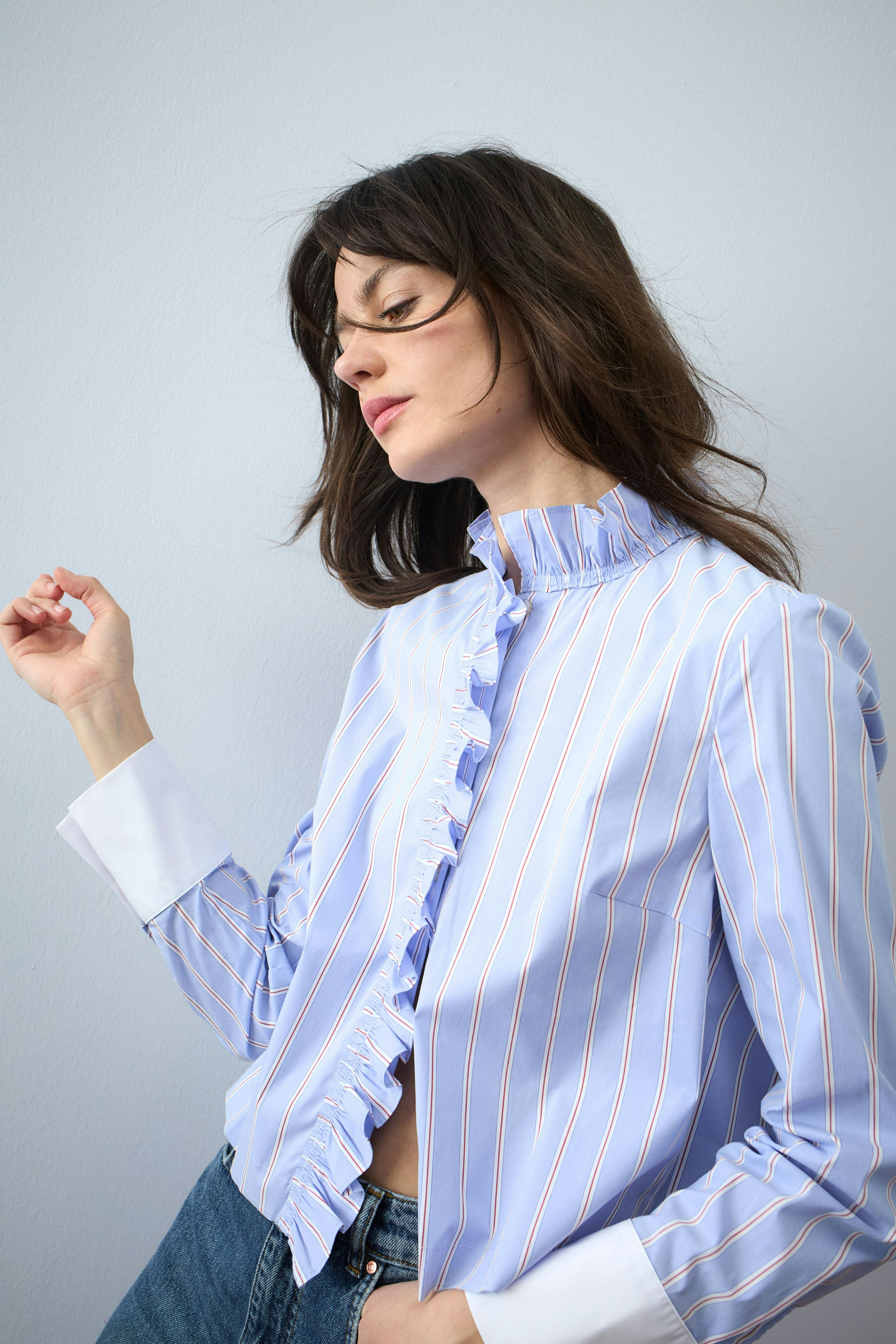 Stylish women's blouse: Woman in a light blue striped blouse with ruffles and casual jeans.