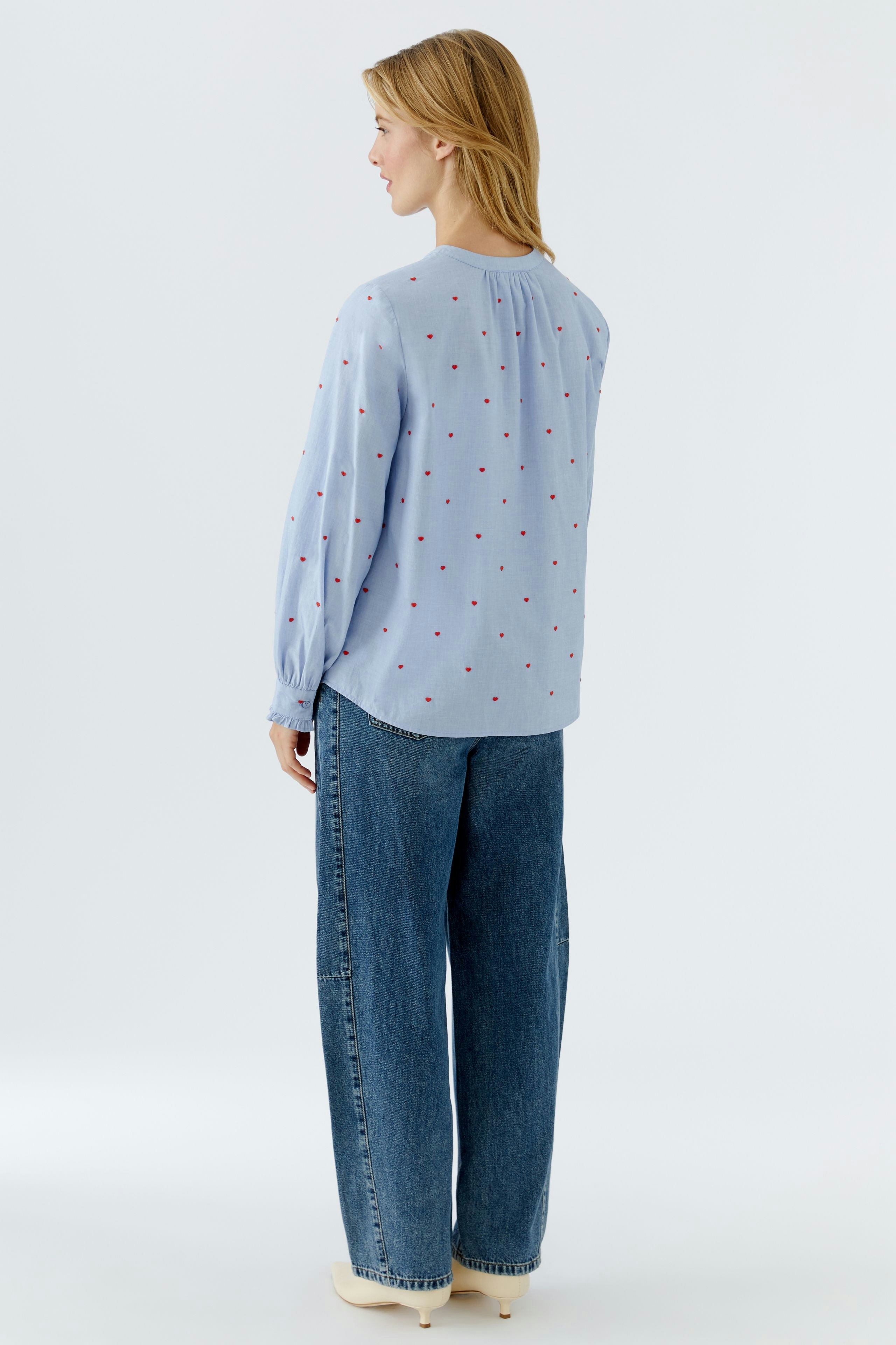 Casual women's blouse: A woman in a light blue blouse with red dots and relaxed-fit jeans.