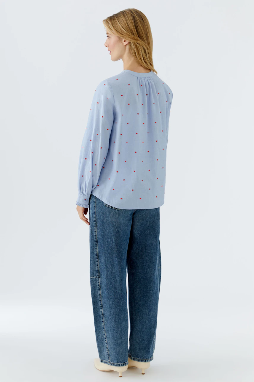 Casual women's blouse: A woman in a light blue blouse with red dots and relaxed-fit jeans.